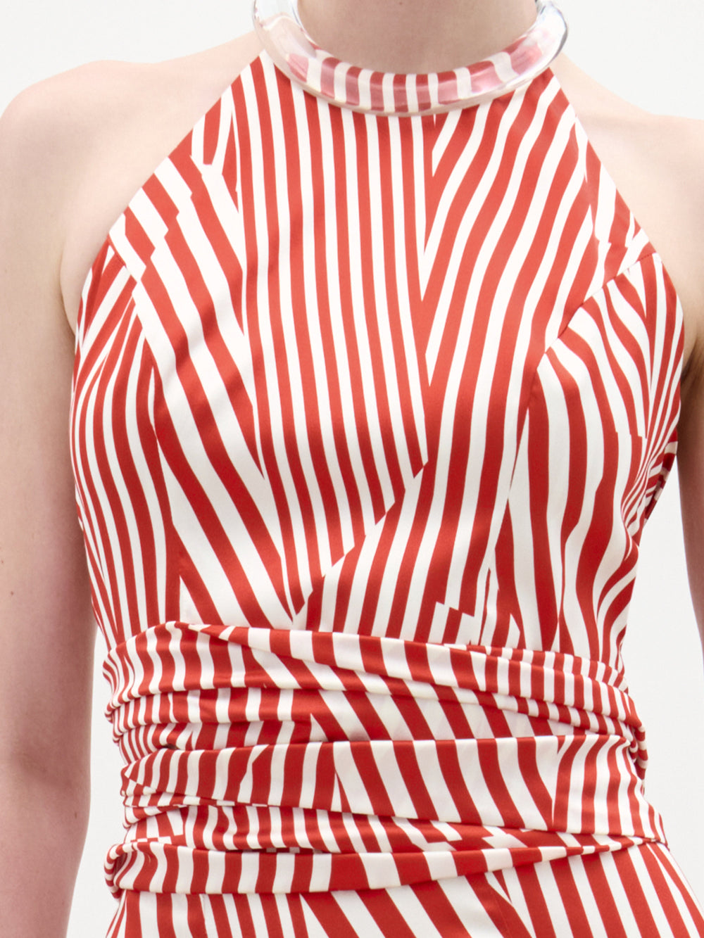 Una persona lleva la blusa Carmela, una blusa sin mangas con rayas diagonales rojas y blancas, estilo halter mujer, escote alto con un claro cuello grueso y detalle fruncido en la cintura, hecho en Colombia.