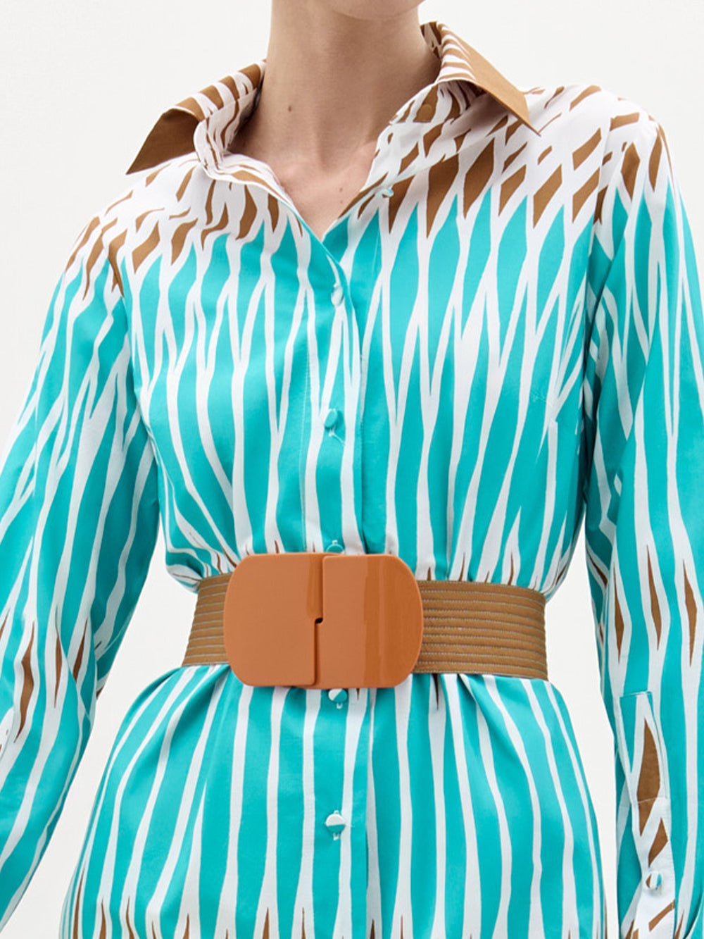 Una persona lleva el Vestido Ronzona -un vestido abotonado con estampado turquesa y blanco y toques marrones- combinado con un cinturón ancho de color tostado y una atrevida hebilla para un look elegante, hecho en Colombia.