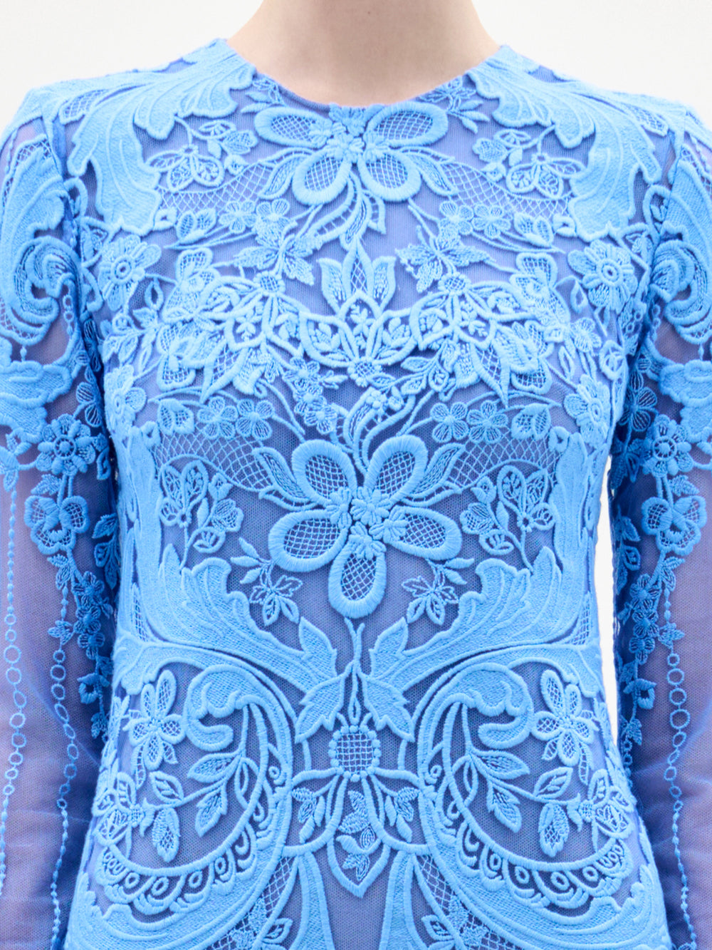 Alguien lleva el vestido Lacey, un vestido azul de manga larga y transparencias con encaje floral y motivos decorativos en la parte delantera y las mangas. La foto está recortada por los hombros, por lo que no se ve la cara.