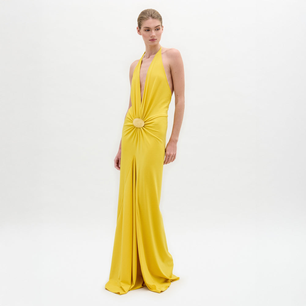 Una persona sobre fondo blanco luce el vestido Aiko, un maxi amarillo sin mangas, largo hasta el suelo, con escote profundo en V, cintura fruncida y adornos circulares. Este elegante vestido está confeccionado en Colombia.
