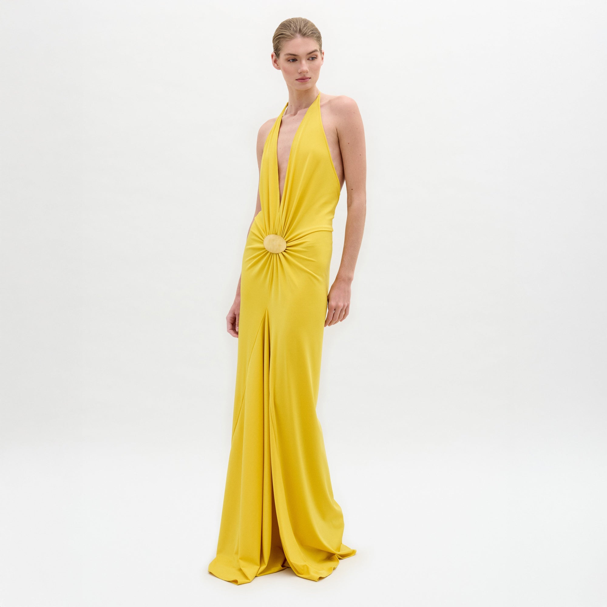 Una persona sobre fondo blanco luce el vestido Aiko, un maxi amarillo sin mangas, largo hasta el suelo, con escote profundo en V, cintura fruncida y adornos circulares. Este elegante vestido está confeccionado en Colombia.