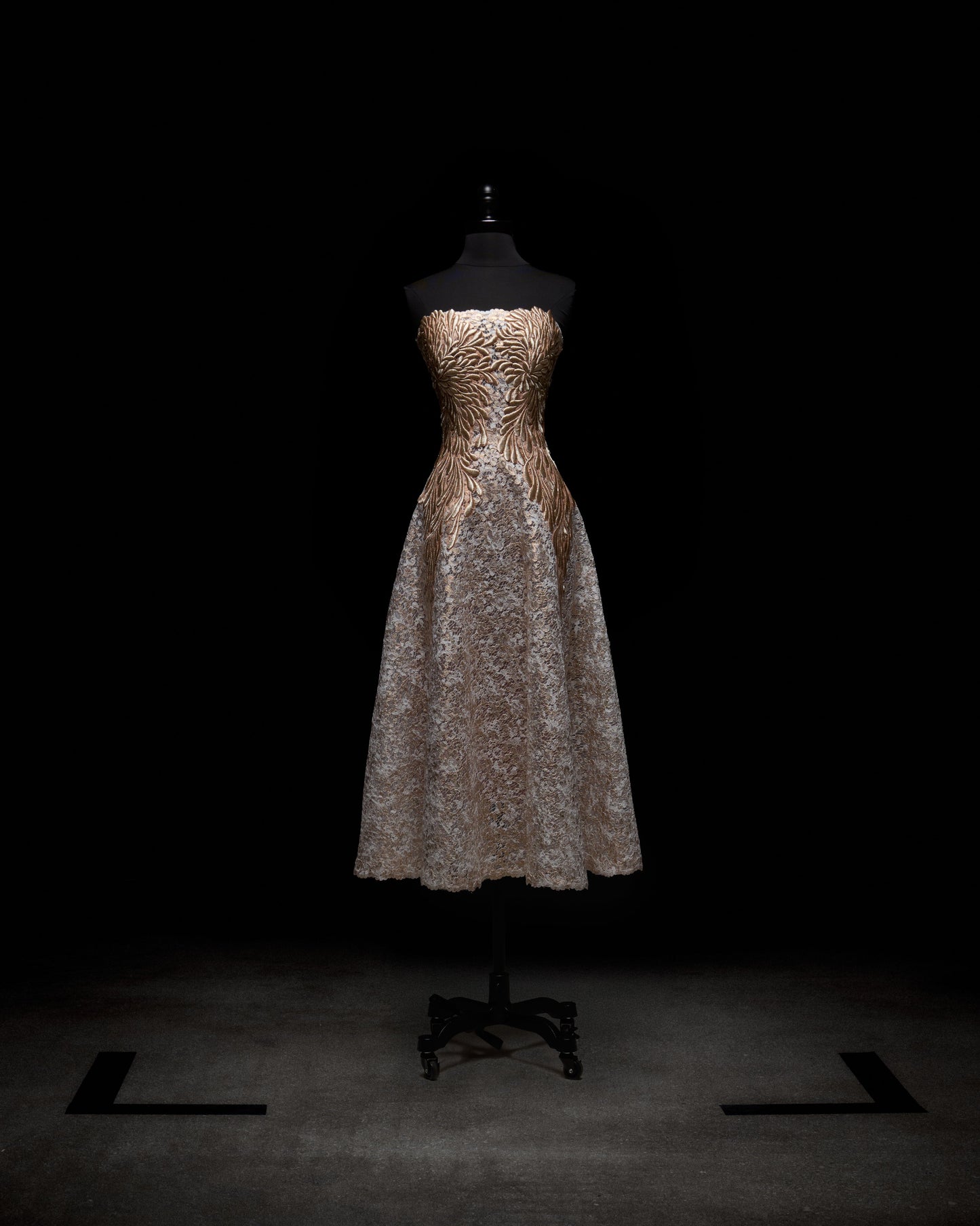 El vestido Alejandra, expuesto sobre un maniquí con luz tenue, luce un diseño sin tirantes con un corpiño con estampado de cebra dorado y negro. La falda de encaje ligero en contraste crea un impactante efecto bicolor sobre el fondo oscuro.