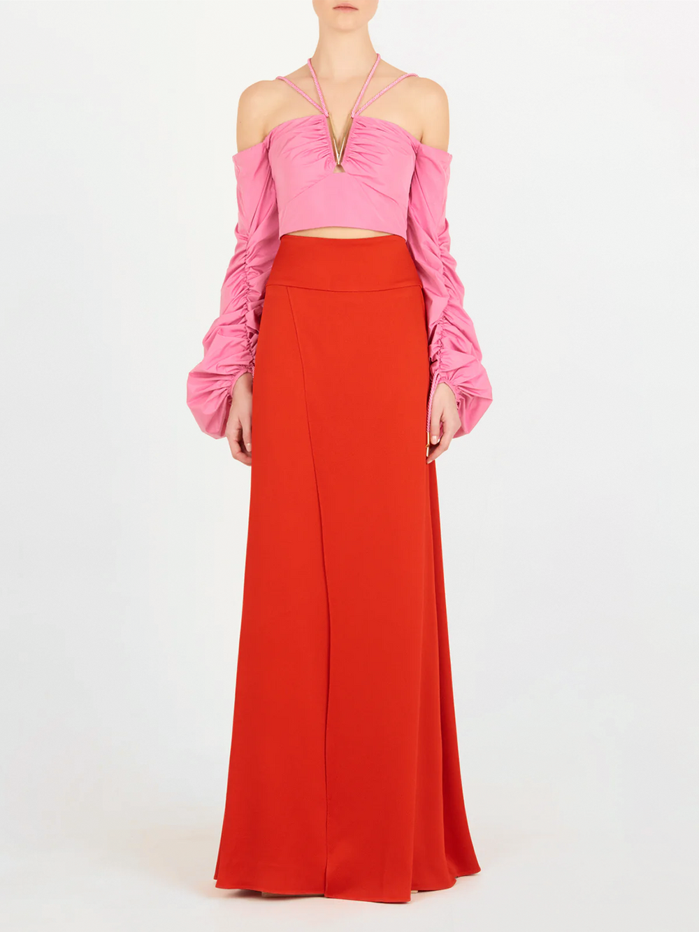 Una persona lleva un crop top rosa sin hombros con mangas fruncidas y escote de tirantes, combinado con la falda de talle alto Pinar Rouge, sobre un fondo blanco liso.