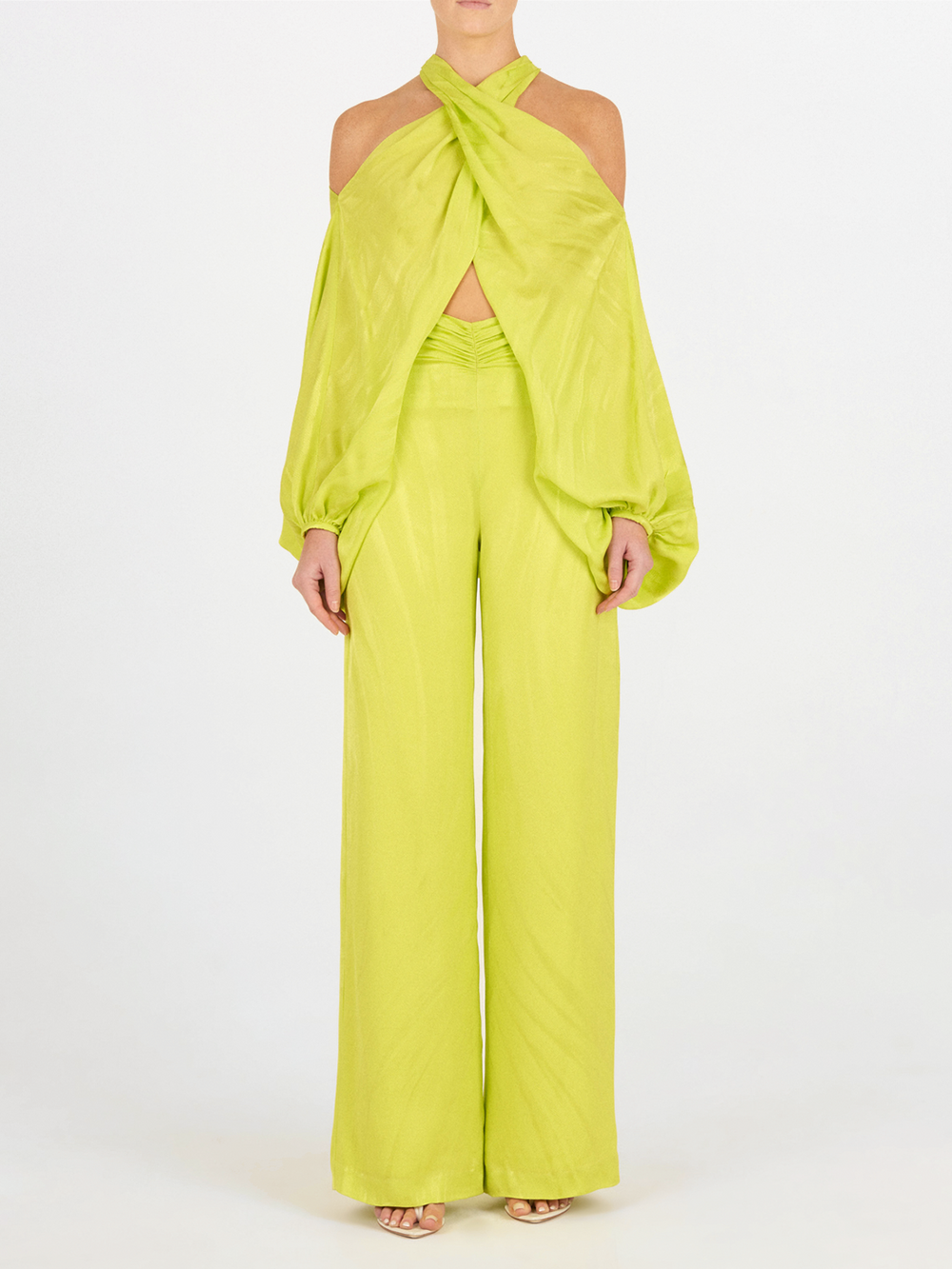 Una persona, de pie y de frente sobre un fondo blanco, lleva el Pantalón Casey Verde Lime, un pantalón de talle alto y pernera ancha en verde lima, combinado con un top sin hombros y zapatos abiertos.