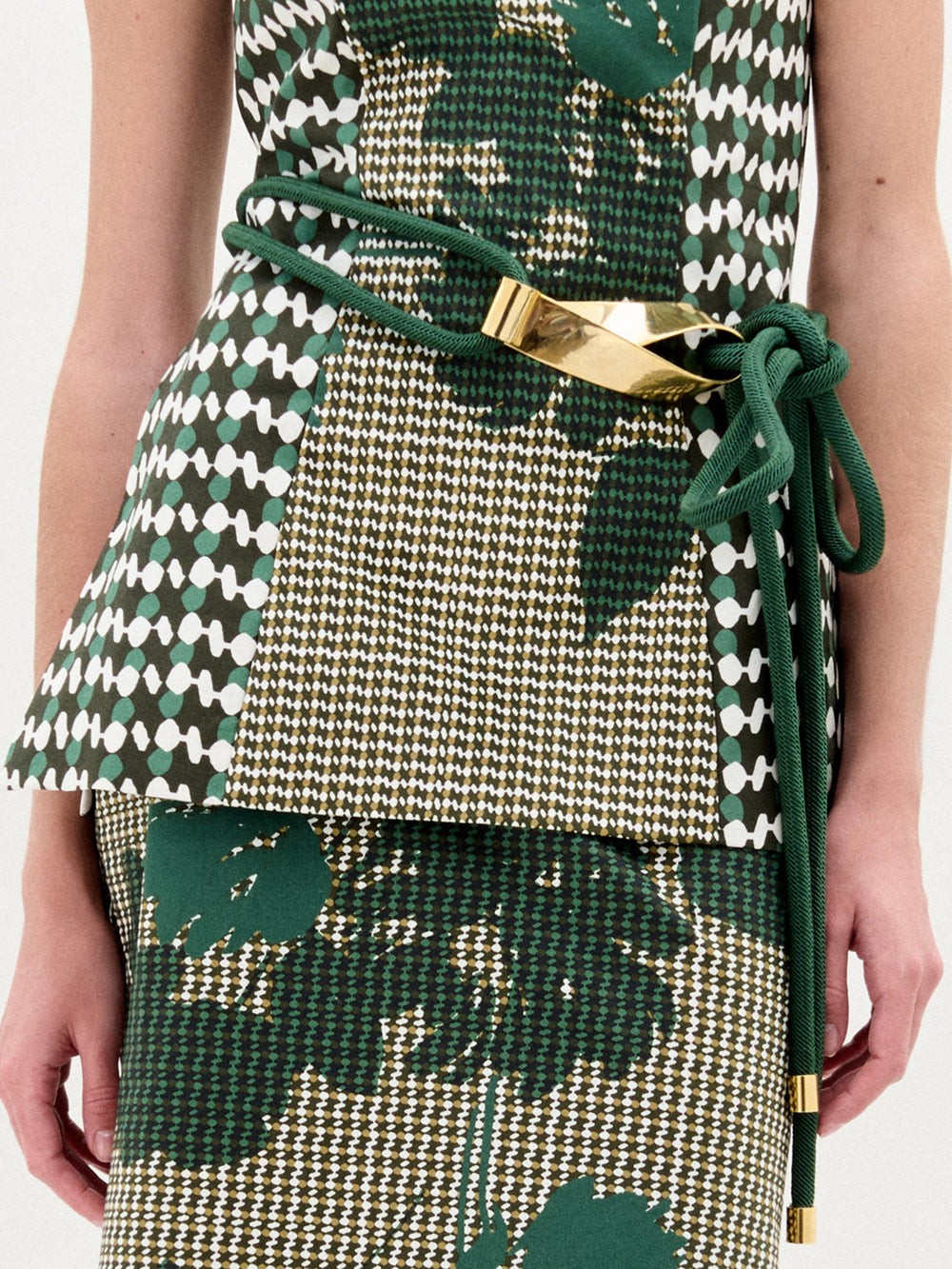 Persona vestida con un traje estampado en verde y blanco, con el cinturón Daiana -con detalles dorados metálicos- atado a la cintura. Sólo se ve el torso y parte del brazo. Este llamativo look está hecho en Colombia.