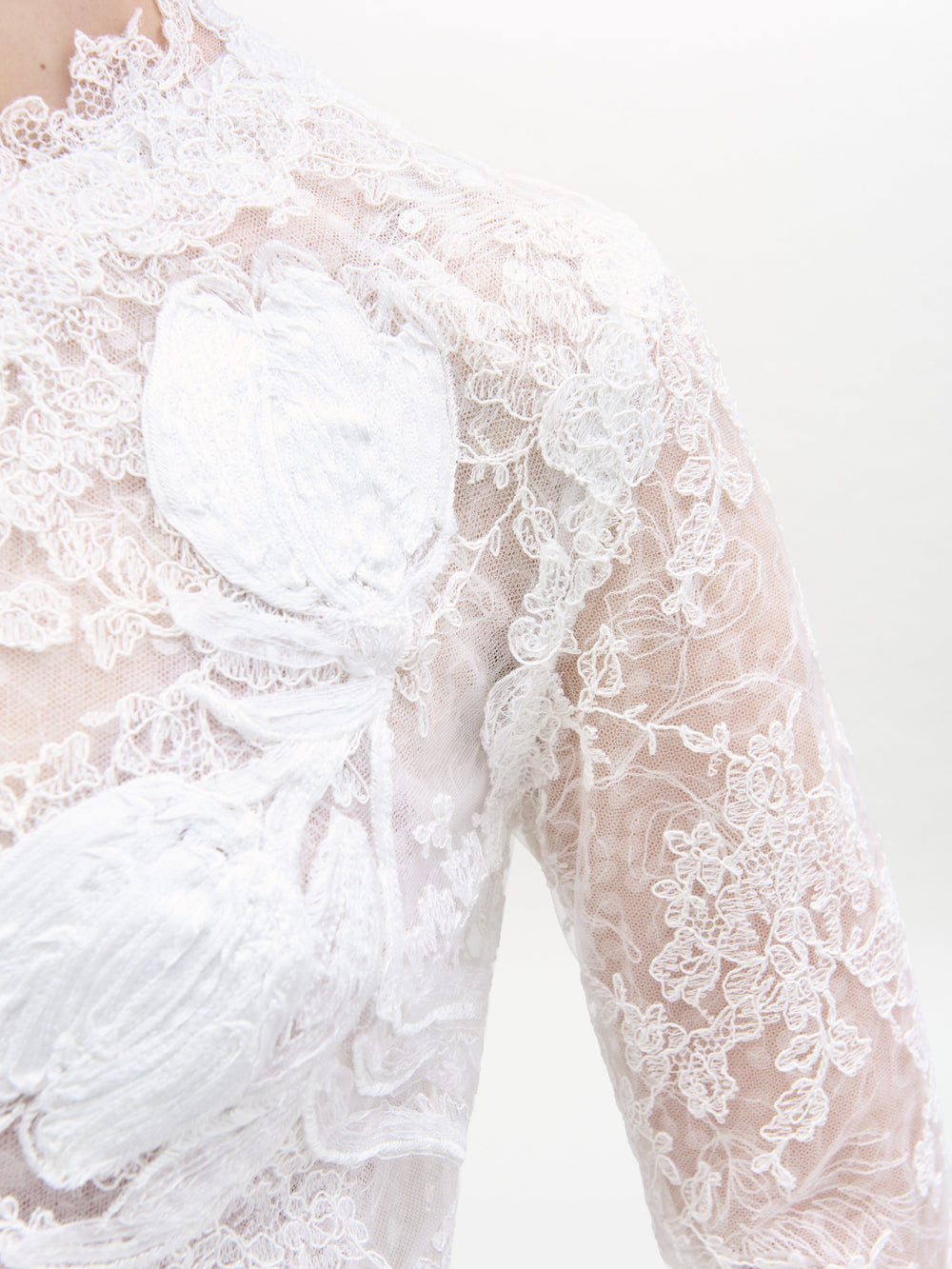 Primer plano del vestido Dava, que luce un intrincado encaje blanco con motivos florales. Esta tela transparente presenta una textura detallada e incluye apliques florales en relieve que aportan profundidad al delicado encaje.