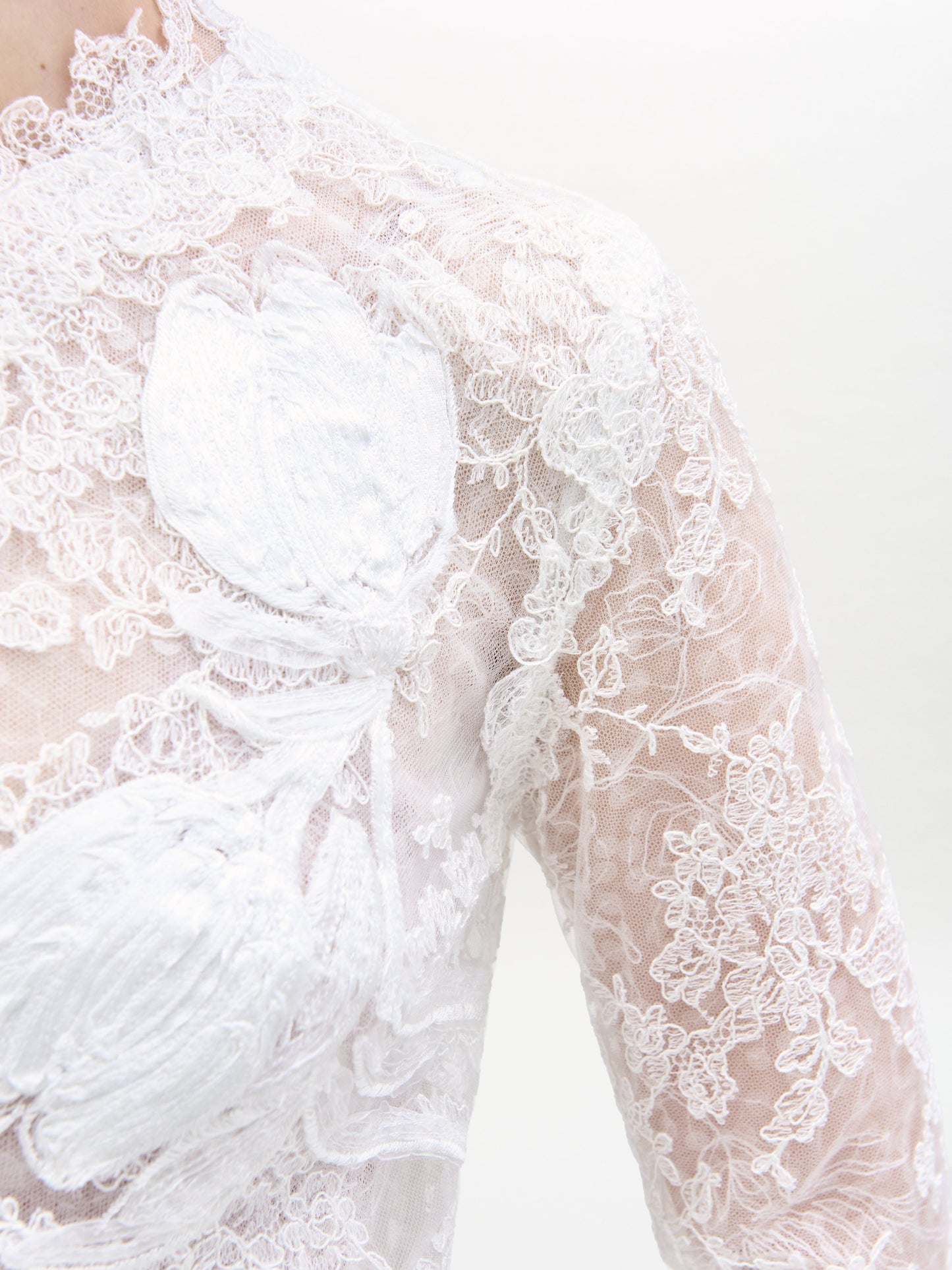 Primer plano del vestido Dava, que luce un intrincado encaje blanco con motivos florales. Esta tela transparente presenta una textura detallada e incluye apliques florales en relieve que aportan profundidad al delicado encaje.