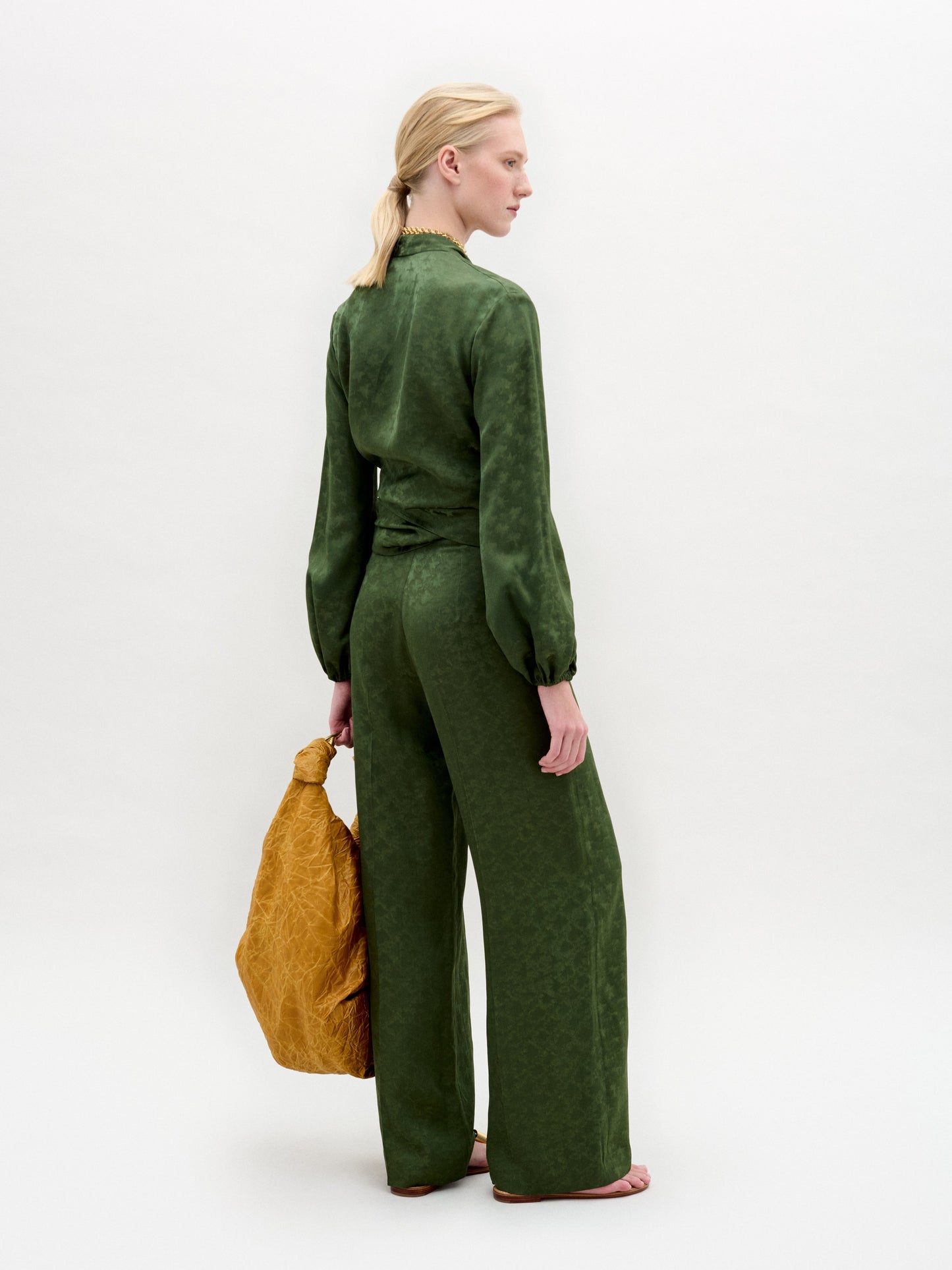 Una persona rubia, descalza sobre fondo blanco, lleva la blusa Elvie con pantalones anchos a juego, fabricados en Colombia, y sostiene un bolso grande de color amarillo mostaza con textura.