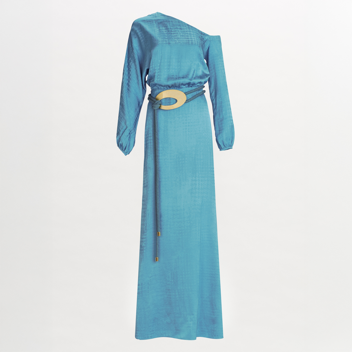 El Vestido Elga es un vestido maxi azul de manga larga y largo hasta el suelo con un sutil estampado texturizado, escote asimétrico y un cinturón ancho de cordón beige con una gran hebilla circular. Se presenta sobre un fondo blanco liso.