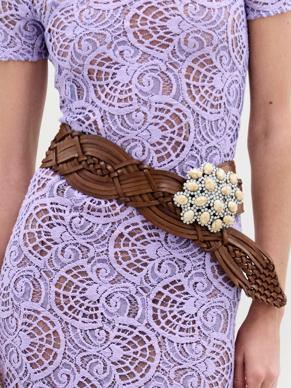 Una persona lleva un vestido de encaje morado claro con el cinturón Eines, un cinturón ancho de cuero con una gran hebilla decorativa adornada con cuentas blancas, fabricado en Italia.