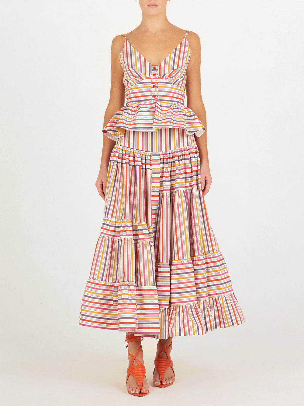 Sobre un fondo liso, una mujer lleva el top Fiorella Top Golden Magenta Stripes de Silvia Tcherassi y una maxifalda a rayas multicolor, combinada con sandalias de tiras naranjas. No se ve su rostro.