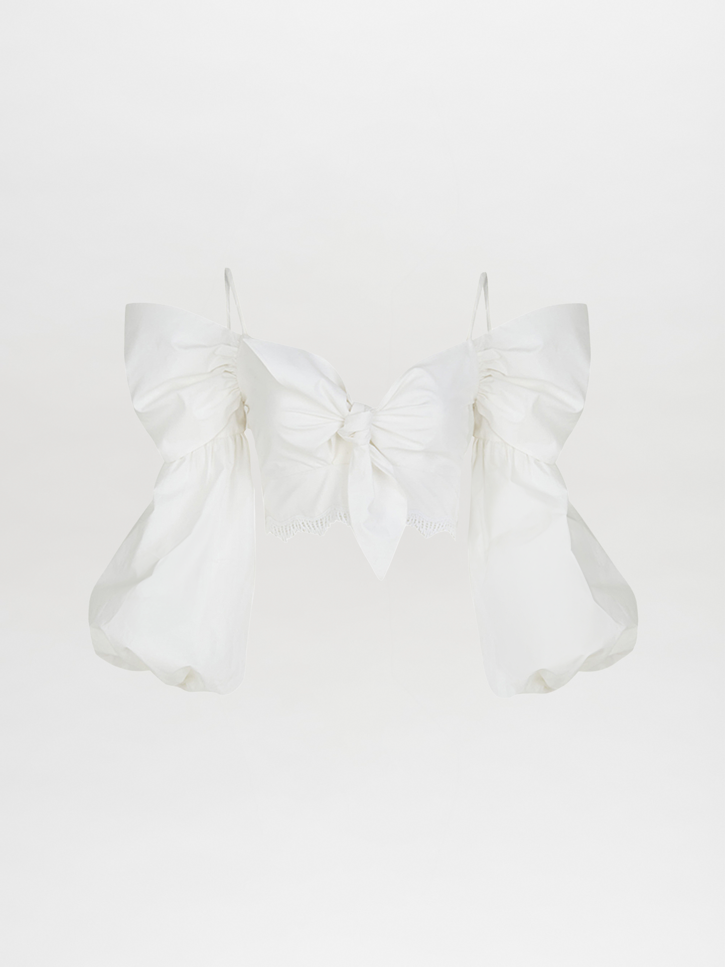 La Blusa Genesis White es una blusa blanca de algodón sin hombros con grandes mangas abullonadas y un lazo central delantero, que se muestra sobre un fondo blanco liso.
