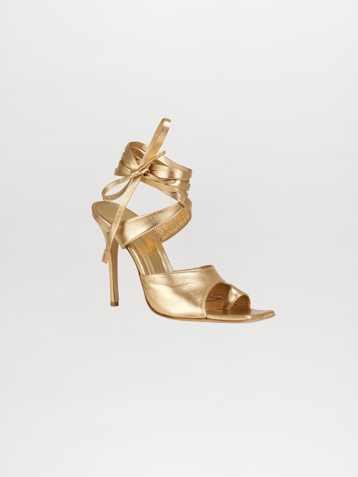 Los Tacones Golda Gold de la colaboración Gia Borghini son unas sandalias de tacón alto con tiras finas y tacón de aguja. Con un detalle de cinta que rodea el tobillo con elegancia, este versátil zapato se ata con un lazo sobre un fondo blanco liso.
