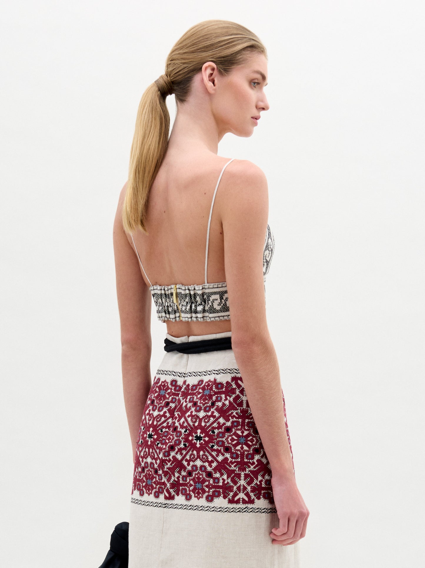 Una mujer con el pelo castaño claro recogido en una coleta baja se ve de espaldas, llevando el Ibbie Top con dibujos en blanco y negro y una falda de cintura alta con bordados geométricos rojos y blancos, hecho en Colombia.