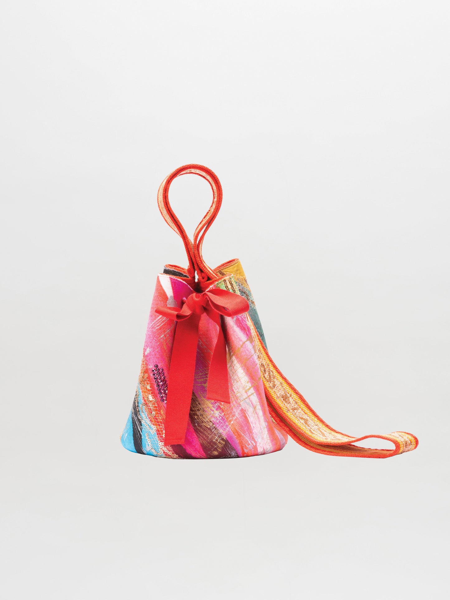 La Mochila Laaput Pequeña es un bolso en forma de cono con un colorido estampado abstracto, acentuado por un lazo rojo y un asa y correa rojas a juego, que se muestra sobre un fondo blanco liso.