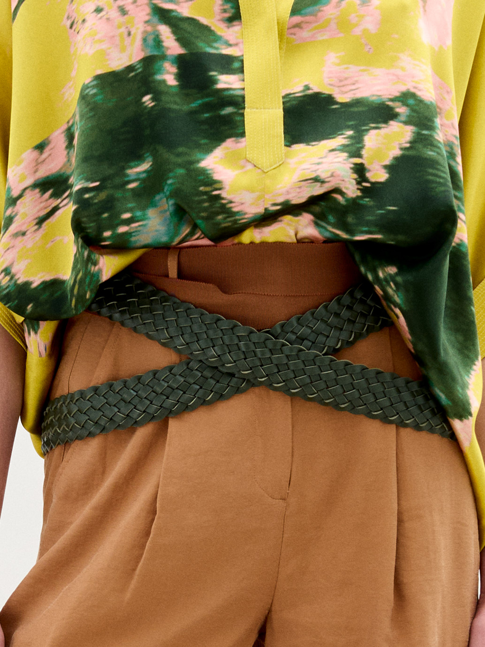 Una persona que lleva pantalones de cintura alta de color canela, el cinturón Lauren cruzado en forma de X y un top estampado de colores verde, amarillo y rosa parcialmente metido por dentro.