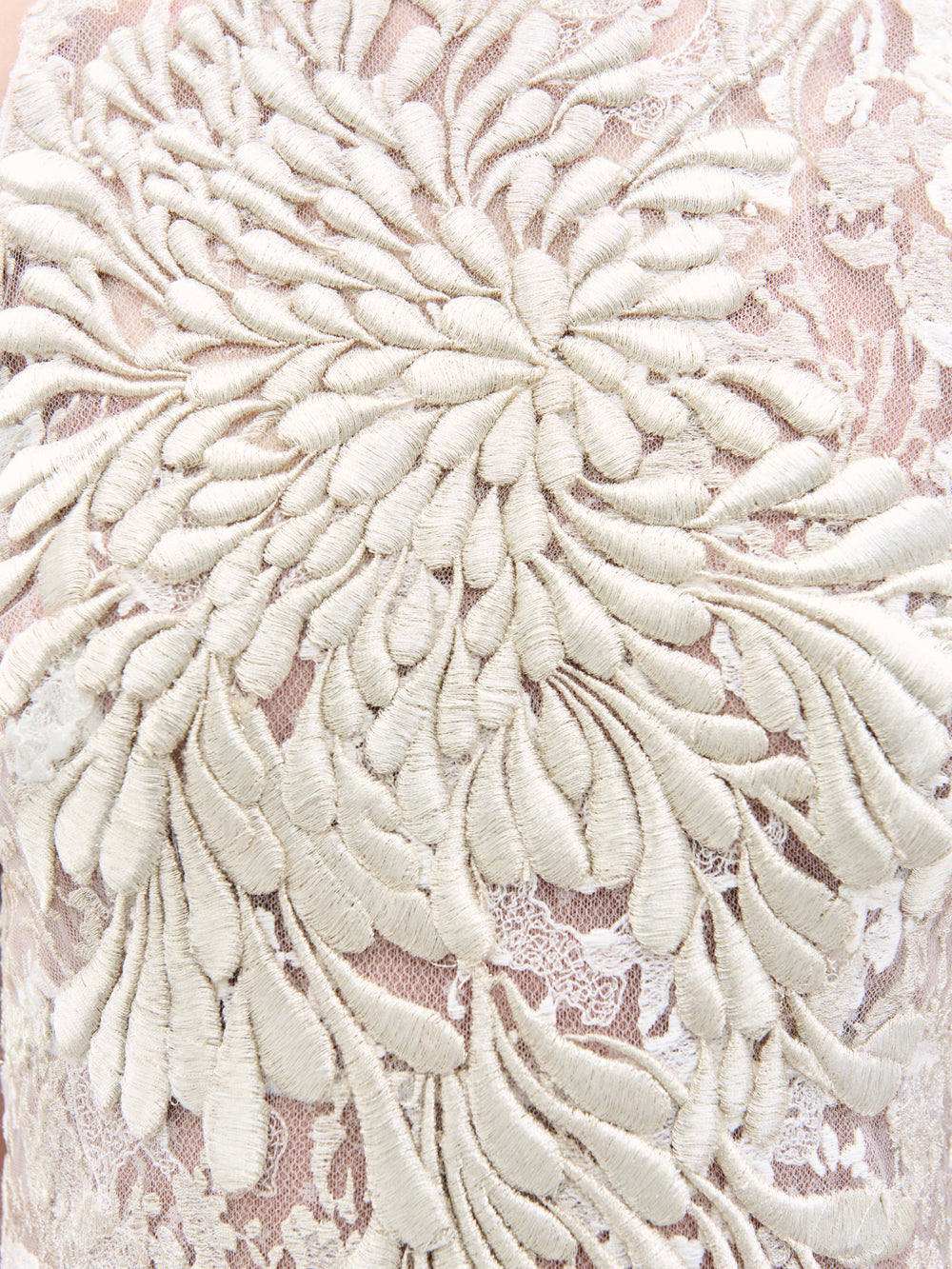 Un primer plano del vestido Levi muestra un intrincado bordado floral, con hilo de color crema que forma grandes pétalos superpuestos sobre un fondo rosa claro transparente para lograr un efecto 3D texturizado.