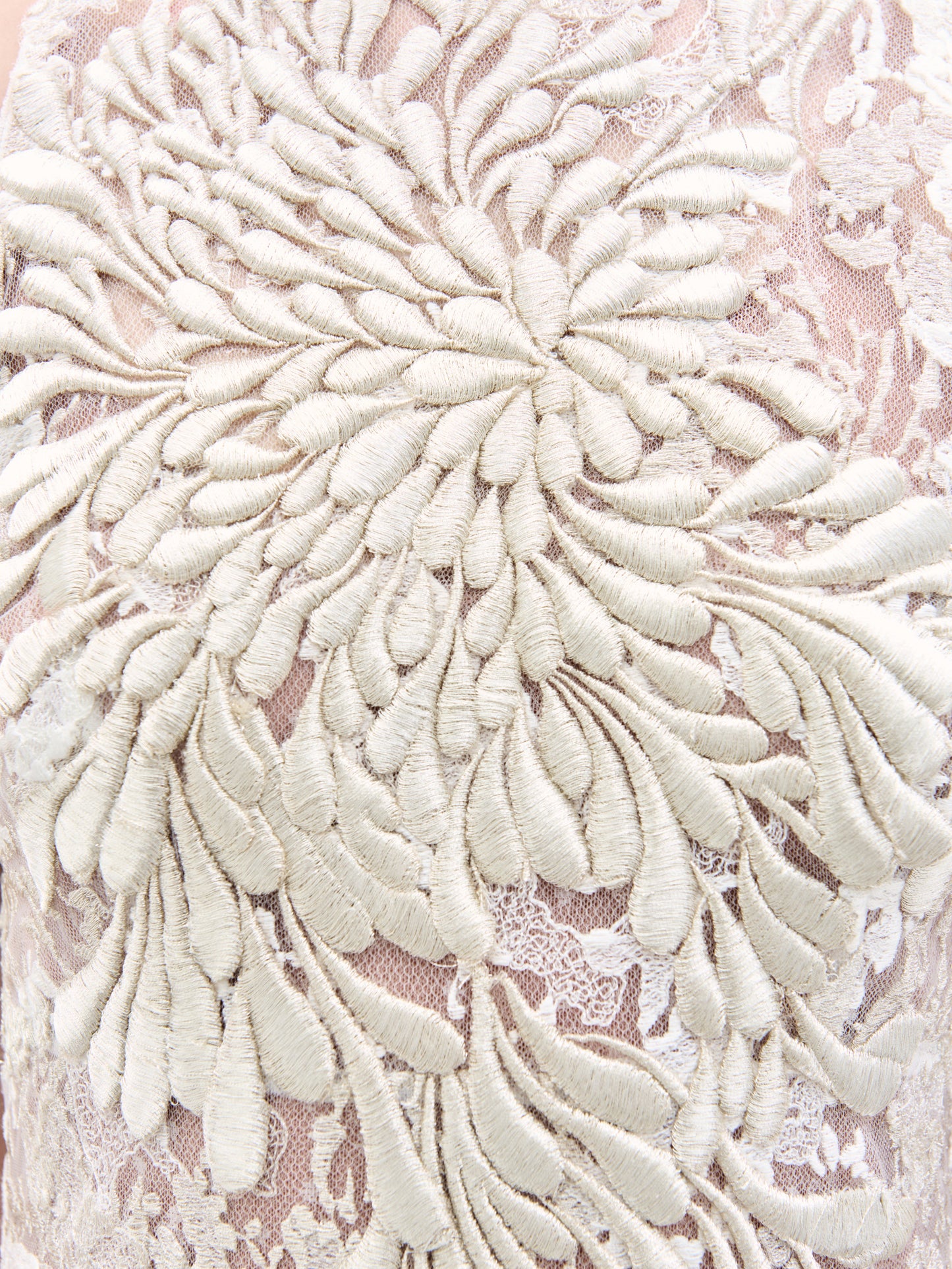 Un primer plano del vestido Levi muestra un intrincado bordado floral, con hilo de color crema que forma grandes pétalos superpuestos sobre un fondo rosa claro transparente para lograr un efecto 3D texturizado.