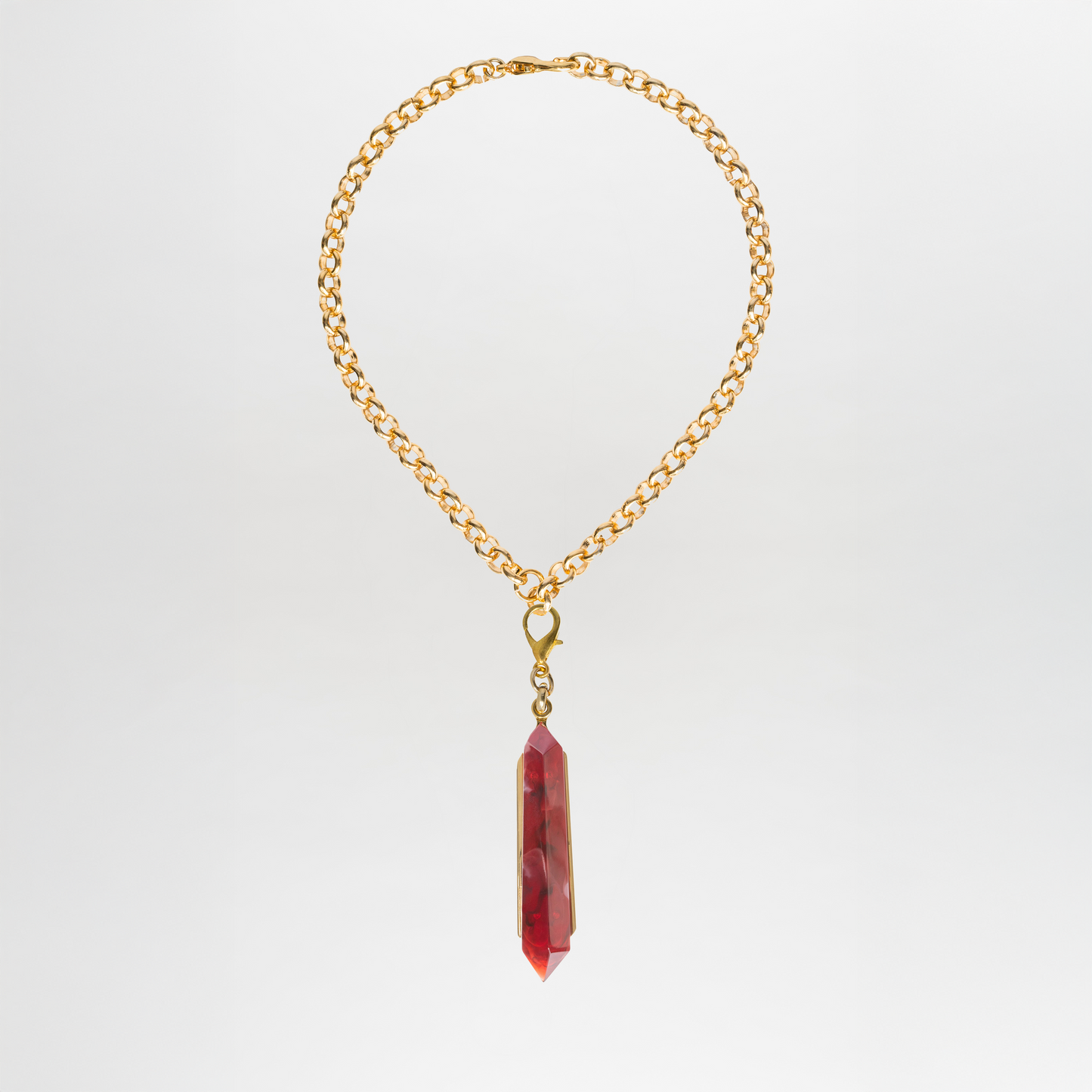 El Collar Mariela es una gargantilla con un único colgante de cristal Petralux® rojo sobre una cadena de latón bañado en oro, que se presenta elegantemente sobre un fondo blanco liso.