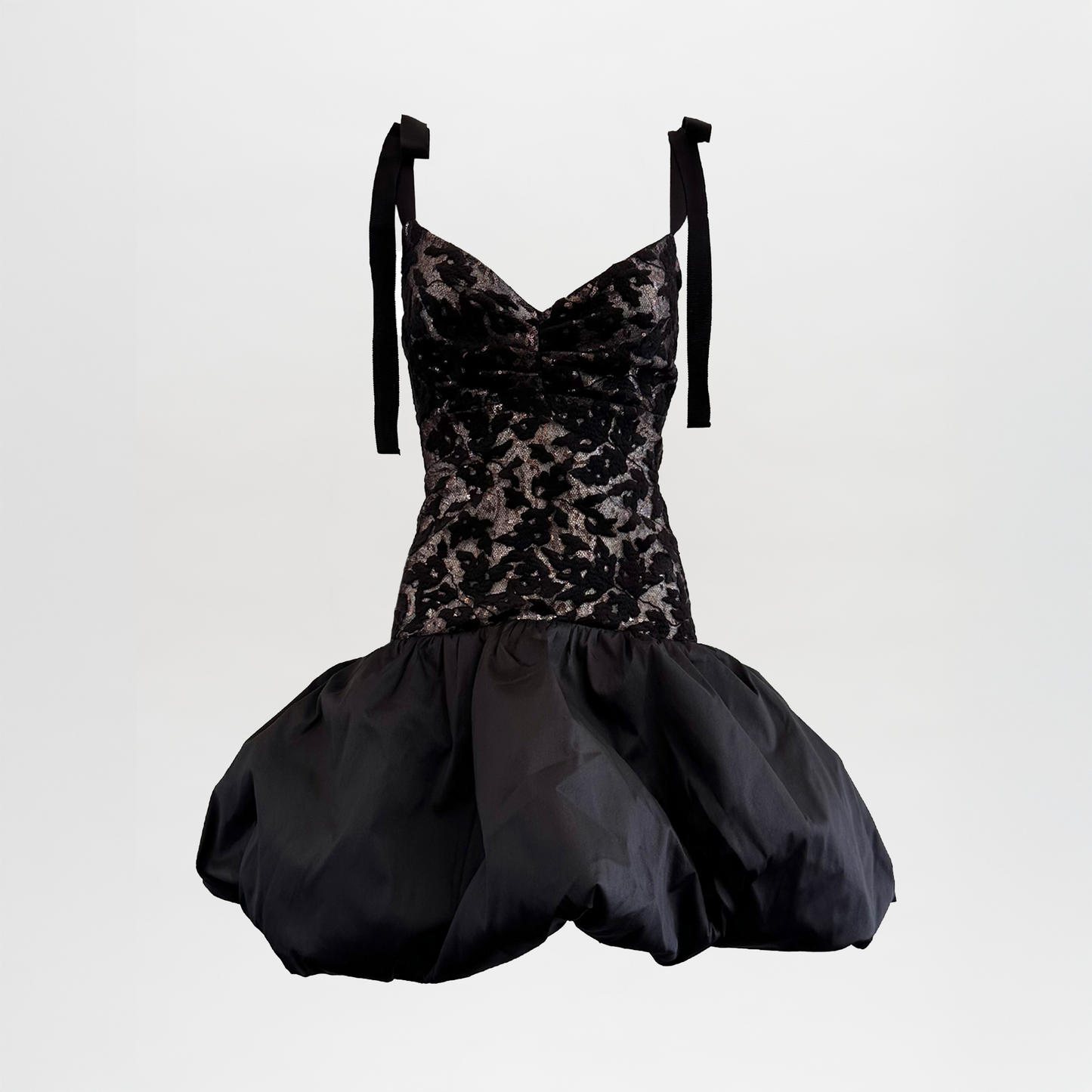 El Vestido Marguerite Black es un minivestido sin mangas que presenta diseños florales de terciopelo en el corpiño, tirantes de cinta y una falda voluminosa con forma de globo, sobre un fondo blanco liso.