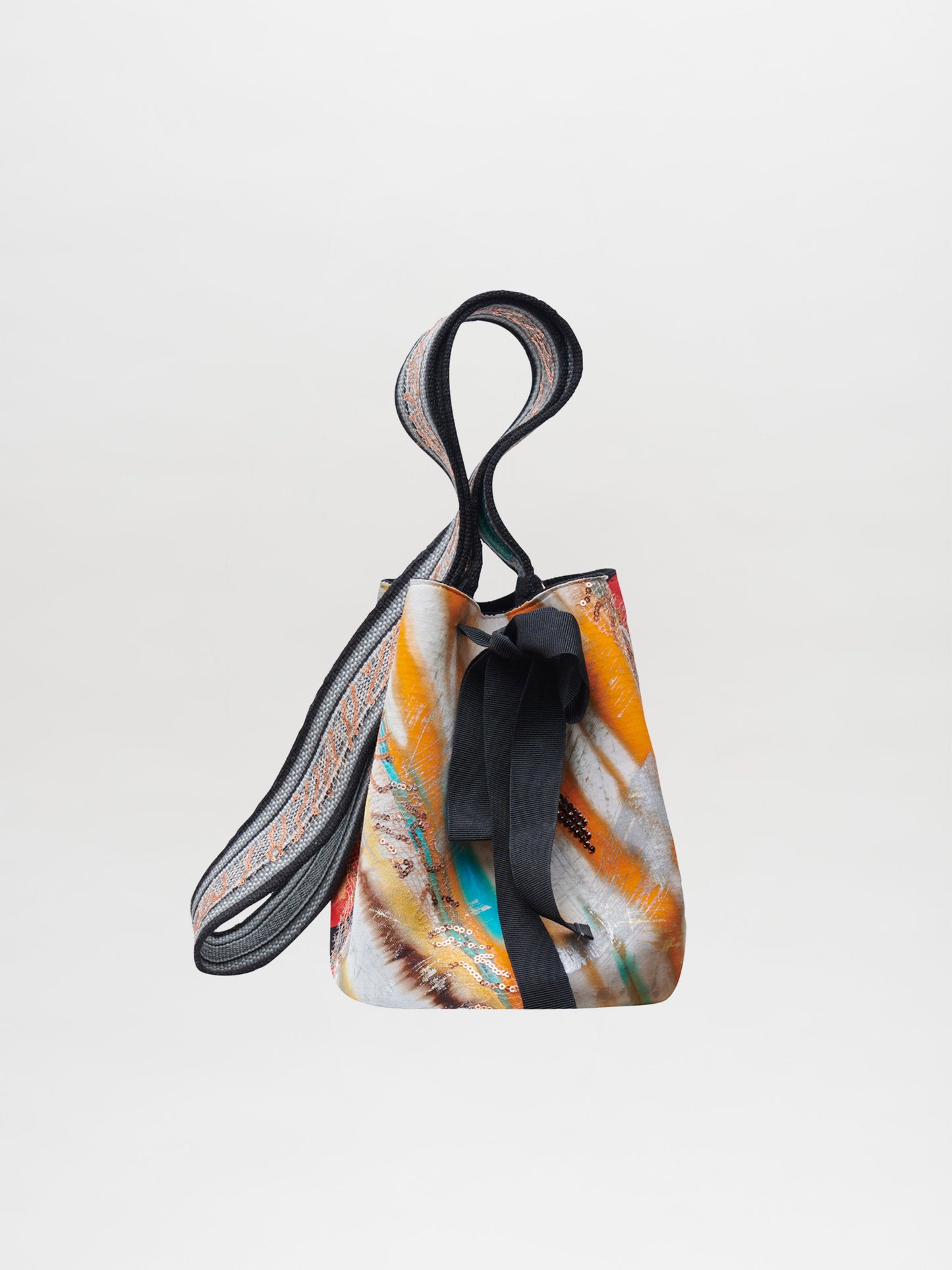 Mochila Laaput Black es un bolso mochila pequeño con un patrón multicolor abstracto, un lazo negro en el frente y una correa de hombro ancha tejida a mano, que se muestra sobre un fondo blanco liso.
