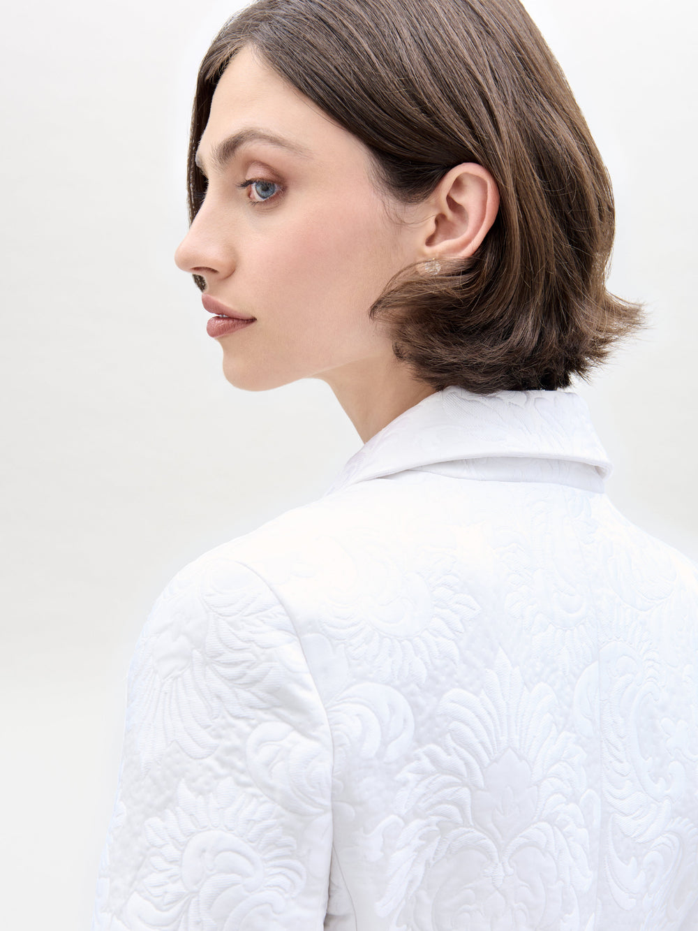 Una mujer de cabello castaño corto luce la Chaqueta Rebeca, un blazer italiano ajustado con solapa en V. Se la ve de perfil sobre un fondo claro y liso, mirando ligeramente por encima del hombro.