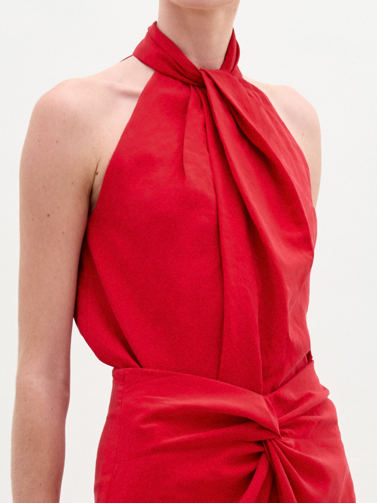 Una persona lleva la blusa Shela, un top sin mangas de color rojo vivo, con fruncidos en el pecho y la cintura, confeccionado en tejido italiano, sobre un fondo claro liso.