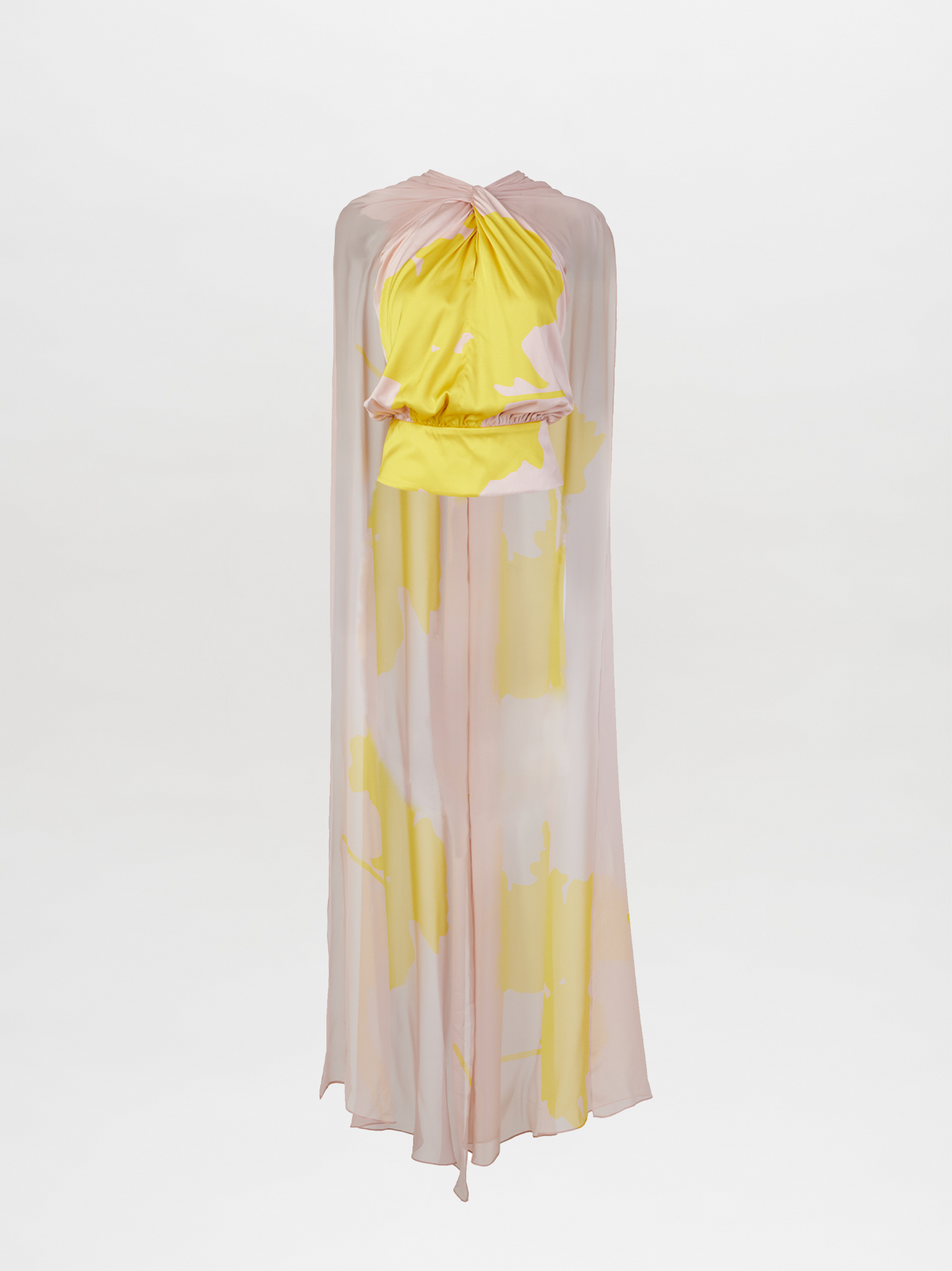 La blusa Vicenta en color amarillo nude presenta una silueta fluida y transparente con un estampado abstracto en rosa pálido y amarillo. Tiene escote alto, frunces en el pecho y una capa superpuesta, perfecta para cualquier ocasión.
