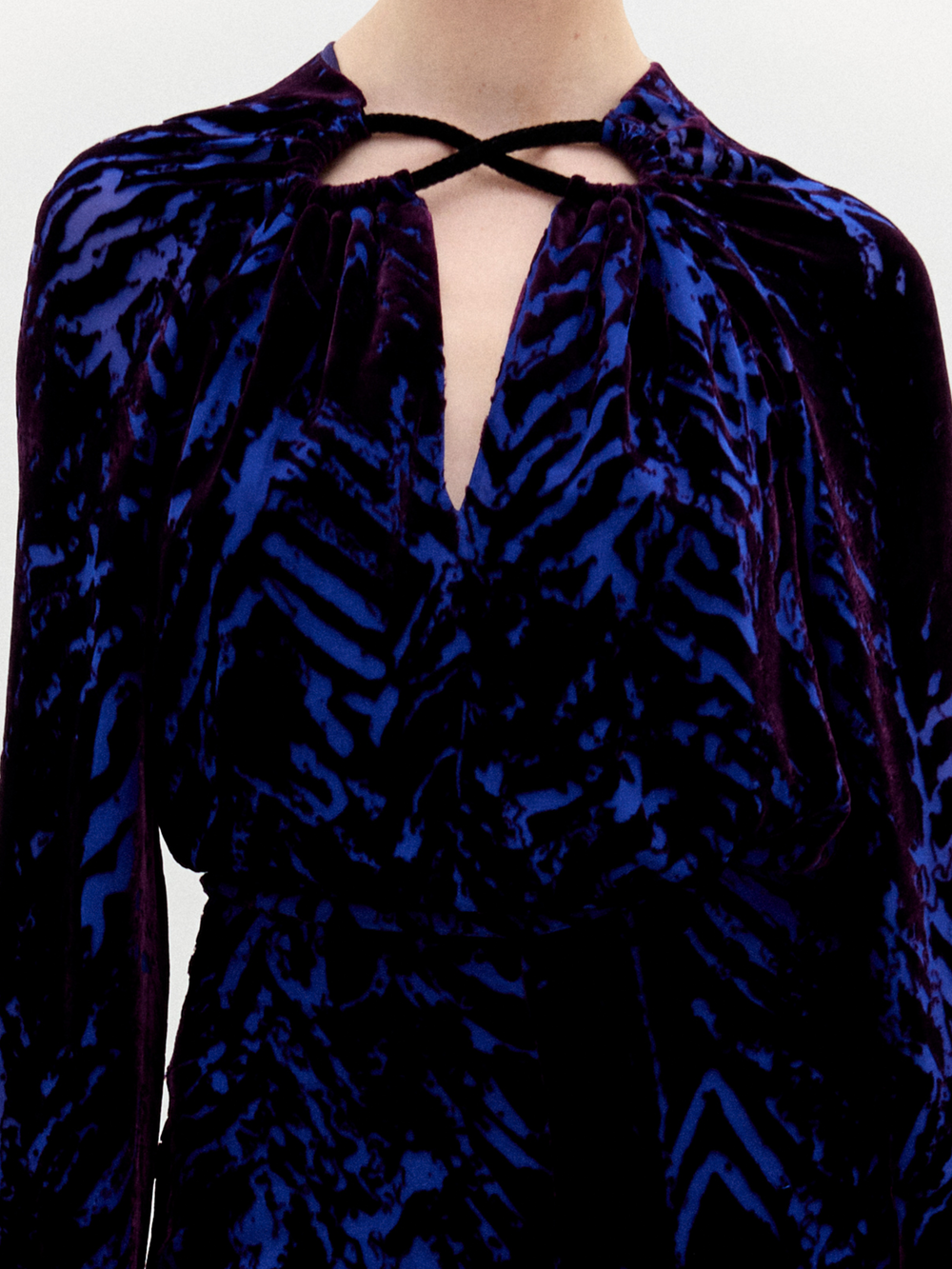 Una persona lleva la blusa Ximena, un top de manga larga con estampado abstracto azul y negro en tela italiana. Tiene escote fruncido, abertura en forma de ojo de cerradura y un fino cordón negro. No se ve la cabeza.