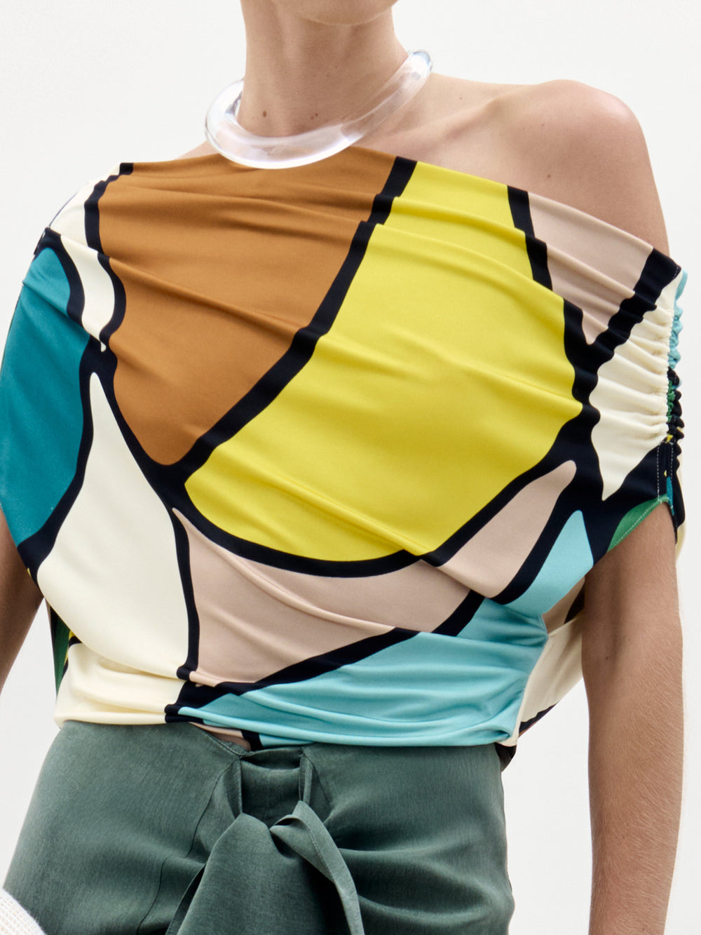 Una persona lleva la Blusa Indiana, un top geométrico asimétrico vibrante con atrevidos contornos negros, confeccionado en tela italiana y hecho en Colombia. Solo se muestra la parte superior del cuerpo sobre un fondo liso.