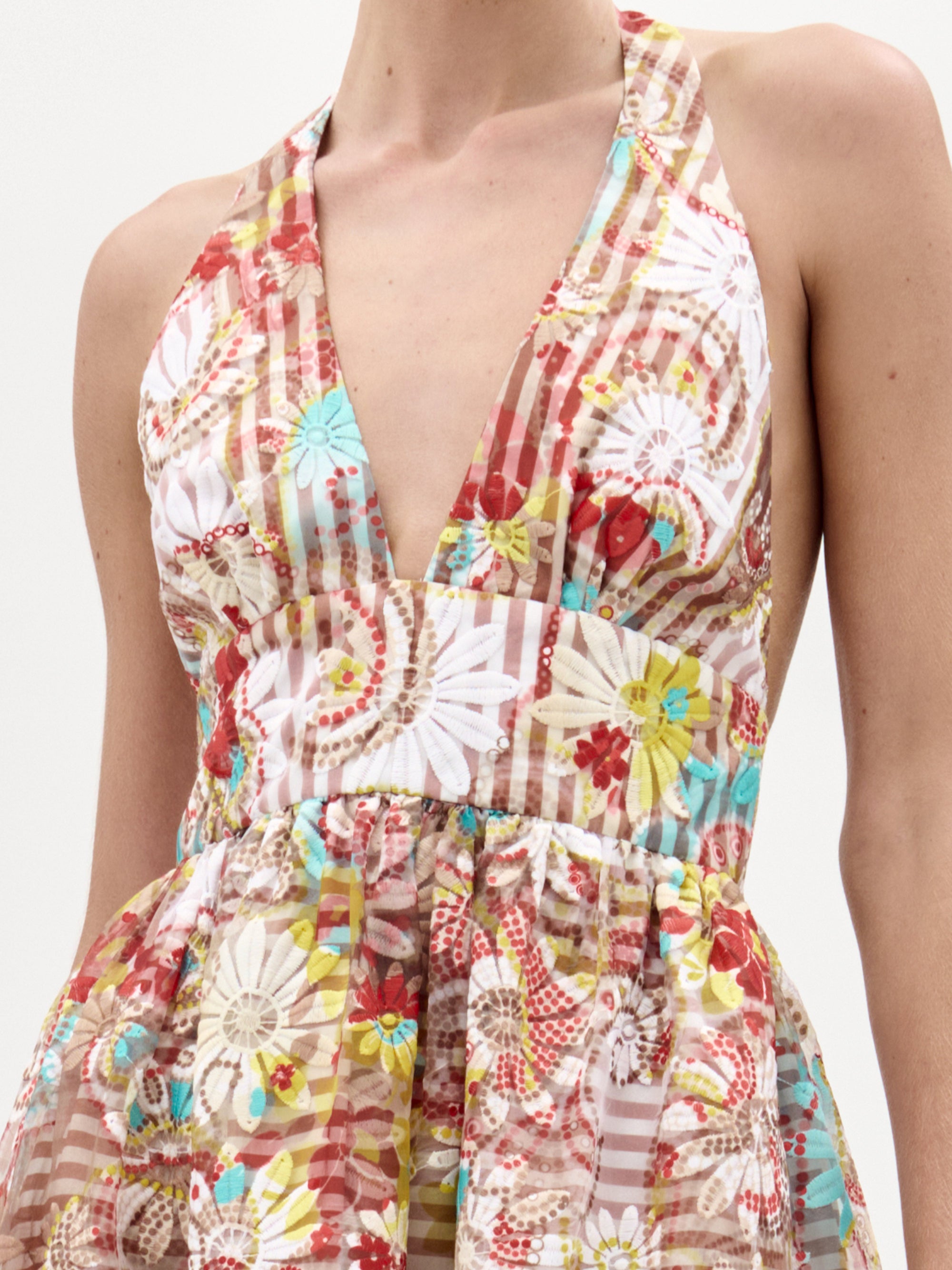 Una persona luce el vestido Kairi, un midi sin mangas de cuello halter con un profundo escote en V y vibrantes motivos florales y geométricos en rojo, marrón, turquesa y amarillo, confeccionado en tela italiana y elaborado en Colombia.