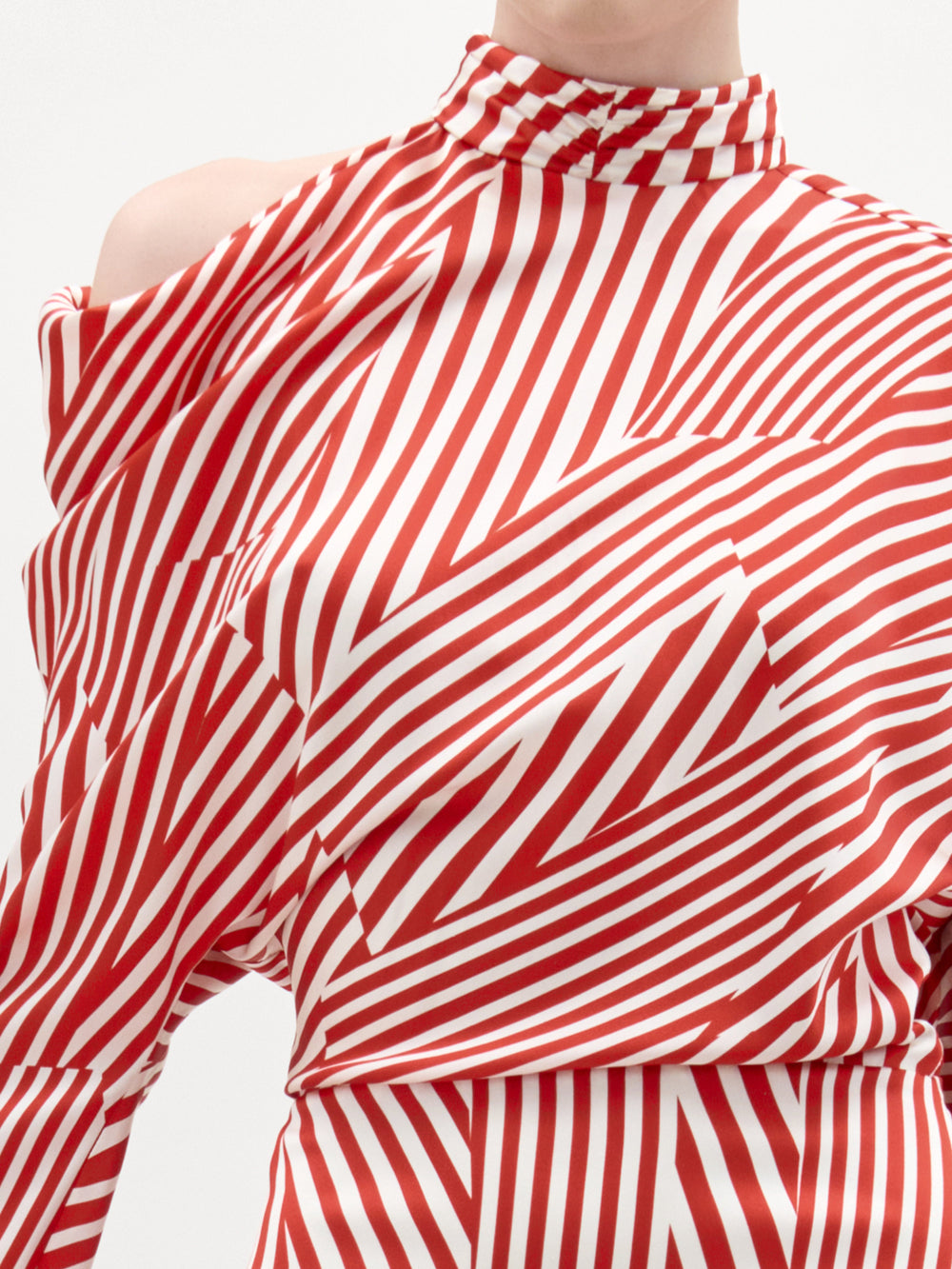 Una persona luce el Vestido Lisa: una pieza de cuello alto, a rayas rojas y blancas, con un diseño asimétrico, un hombro al descubierto y confeccionada en suave seda. Las rayas geométricas aportan un toque único al tejido.