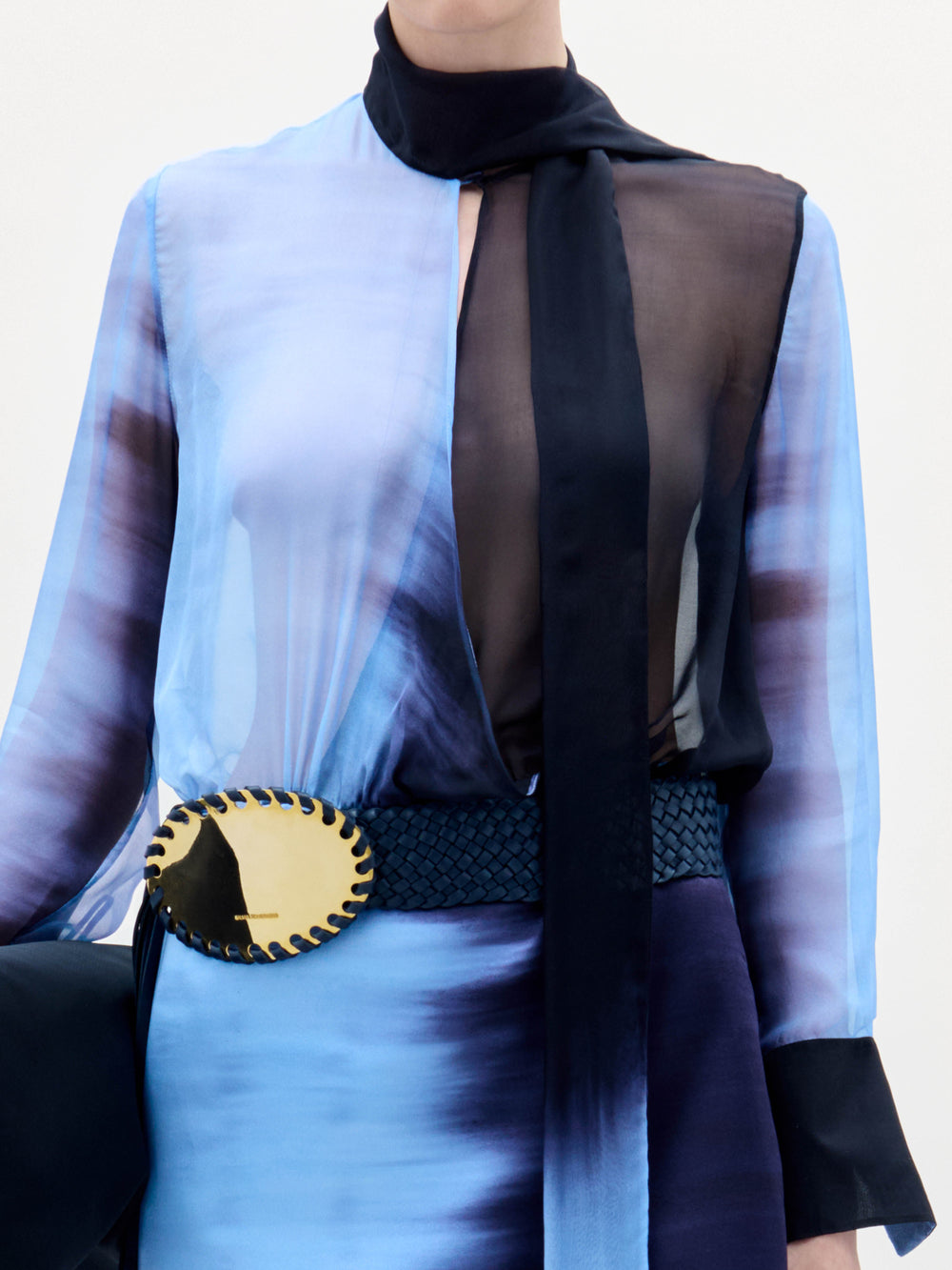 Alguien lleva el vestido Imelda, de color azul y negro, con un profundo escote en V, acentuado por una gran hebilla de cinturón negra y dorada, y un largo pañuelo negro alrededor del cuello. La foto está recortada por los hombros y las rodillas.