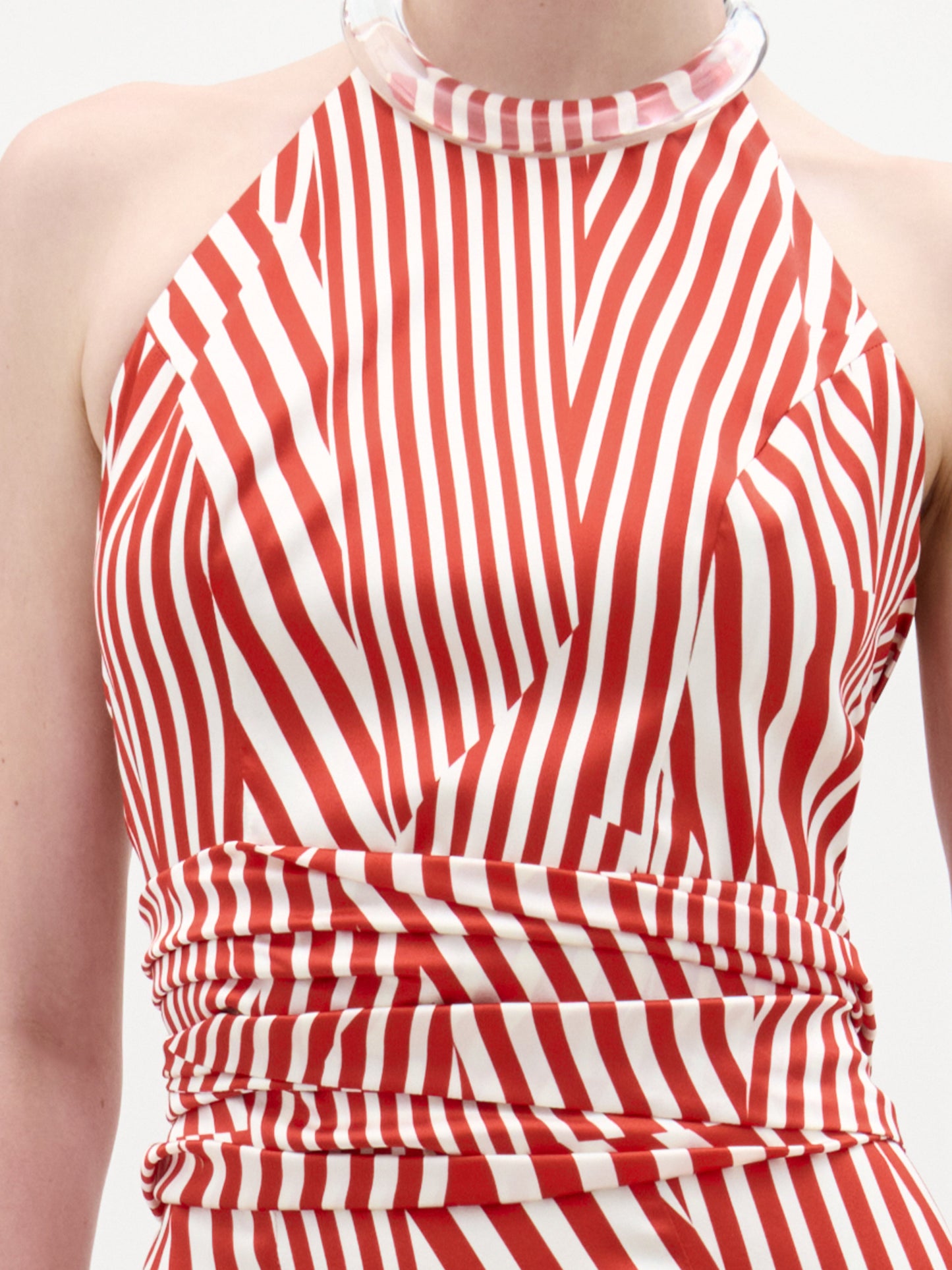 Una persona lleva la blusa Carmela, una blusa sin mangas con rayas diagonales rojas y blancas, estilo halter mujer, escote alto con un claro cuello grueso y detalle fruncido en la cintura, hecho en Colombia.
