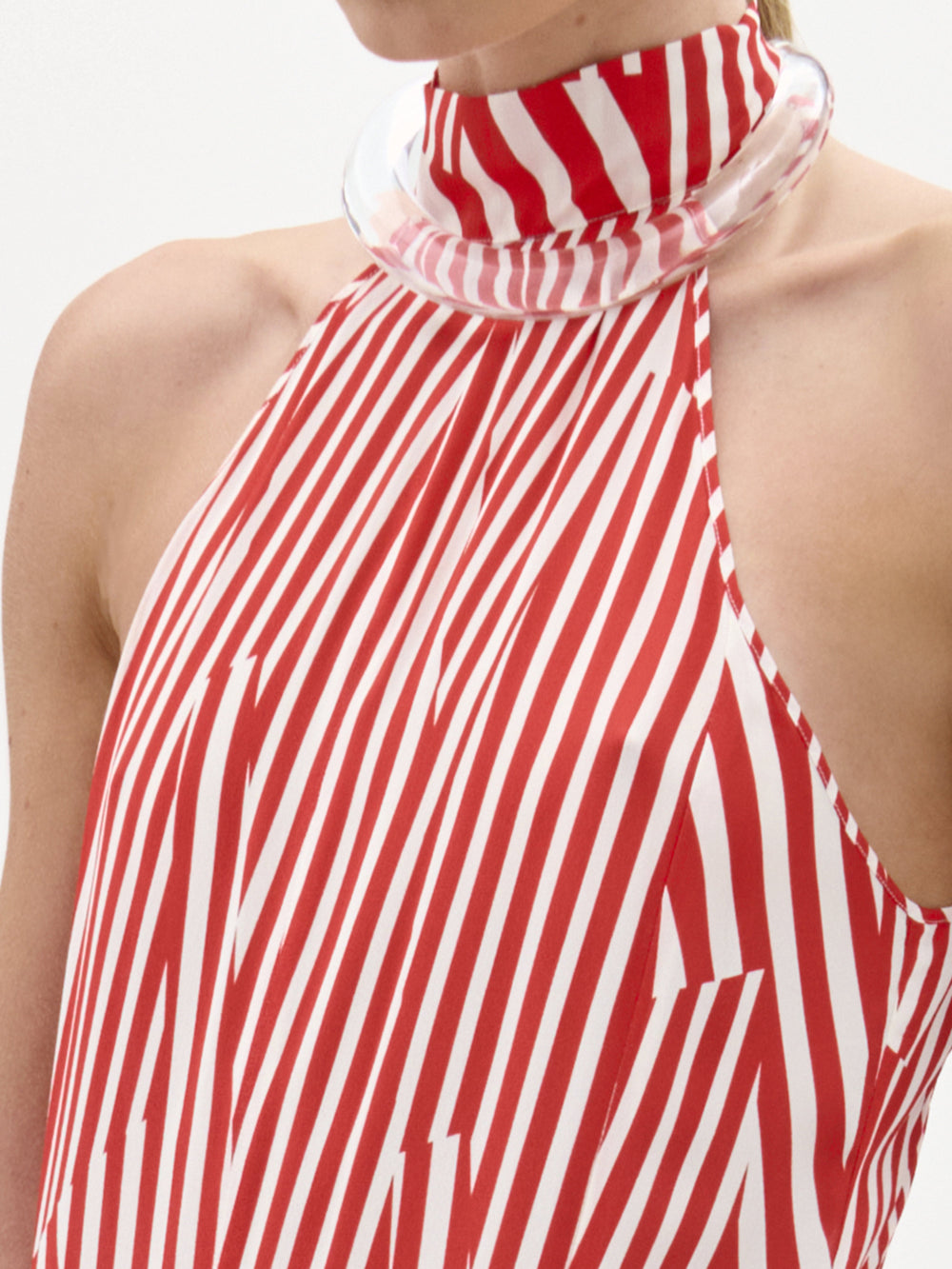 Una persona con el Vestido Koa: un top sin mangas de rayas rojas y blancas y cuello alto, con un claro y grueso cuello circular y líneas diagonales y verticales. Sólo se muestra la parte superior del torso. Prenda hecha en Colombia.