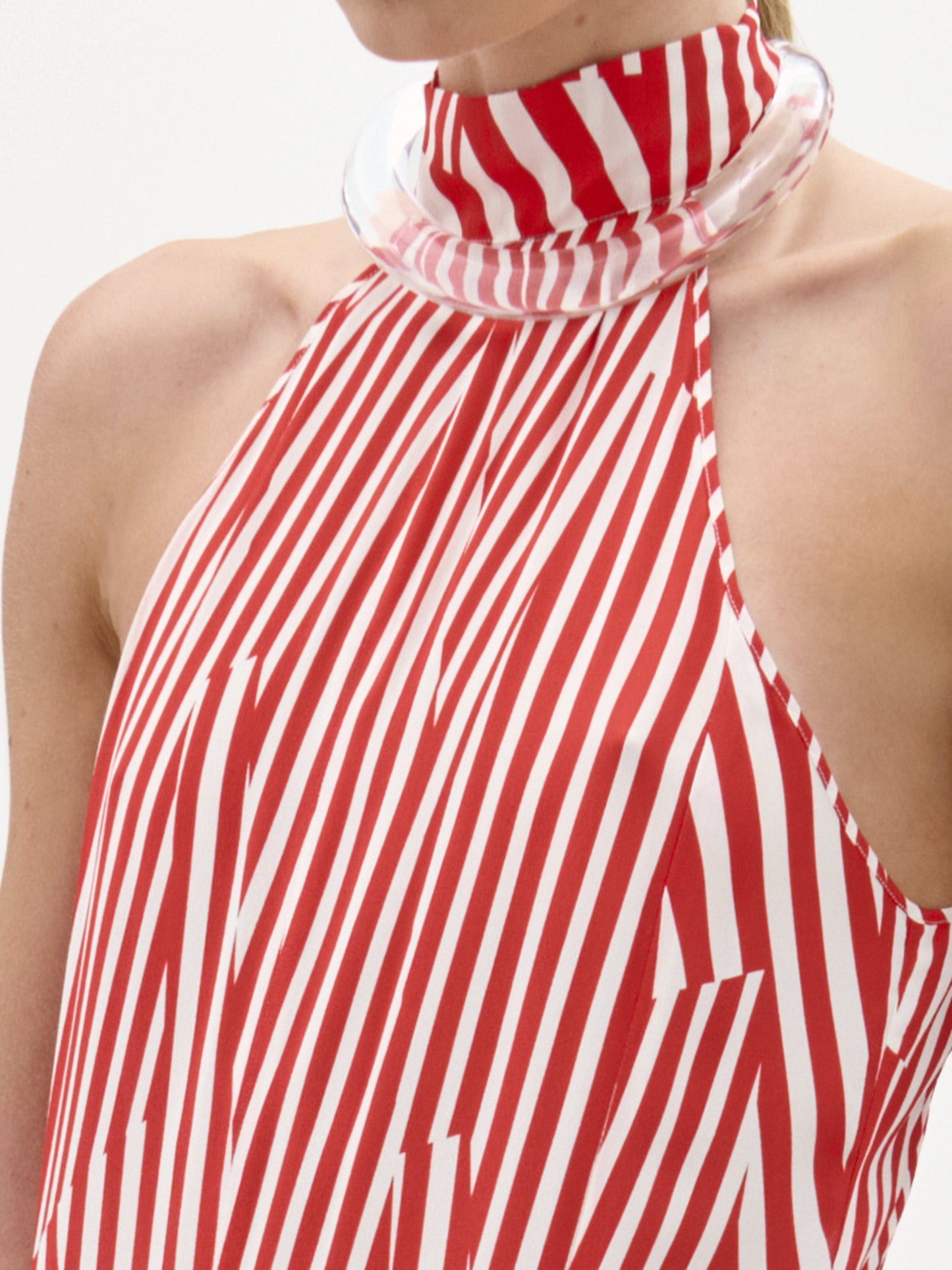 Una persona con el Vestido Koa: un top sin mangas de rayas rojas y blancas y cuello alto, con un claro y grueso cuello circular y líneas diagonales y verticales. Sólo se muestra la parte superior del torso. Prenda hecha en Colombia.