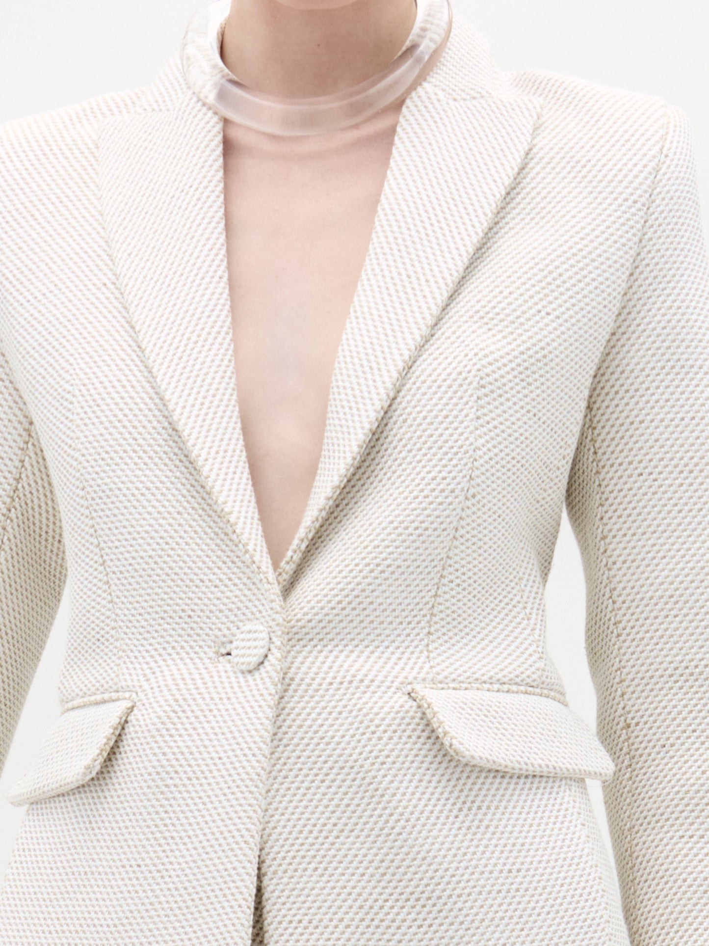 Una persona viste la Chaqueta Rebeca, un blazer color crema entallado con solapas de muesca, bolsillos con solapa y un solo botón. Su silueta estructurada acentúa la parte superior del pecho y el cuello sobre un fondo liso y claro.