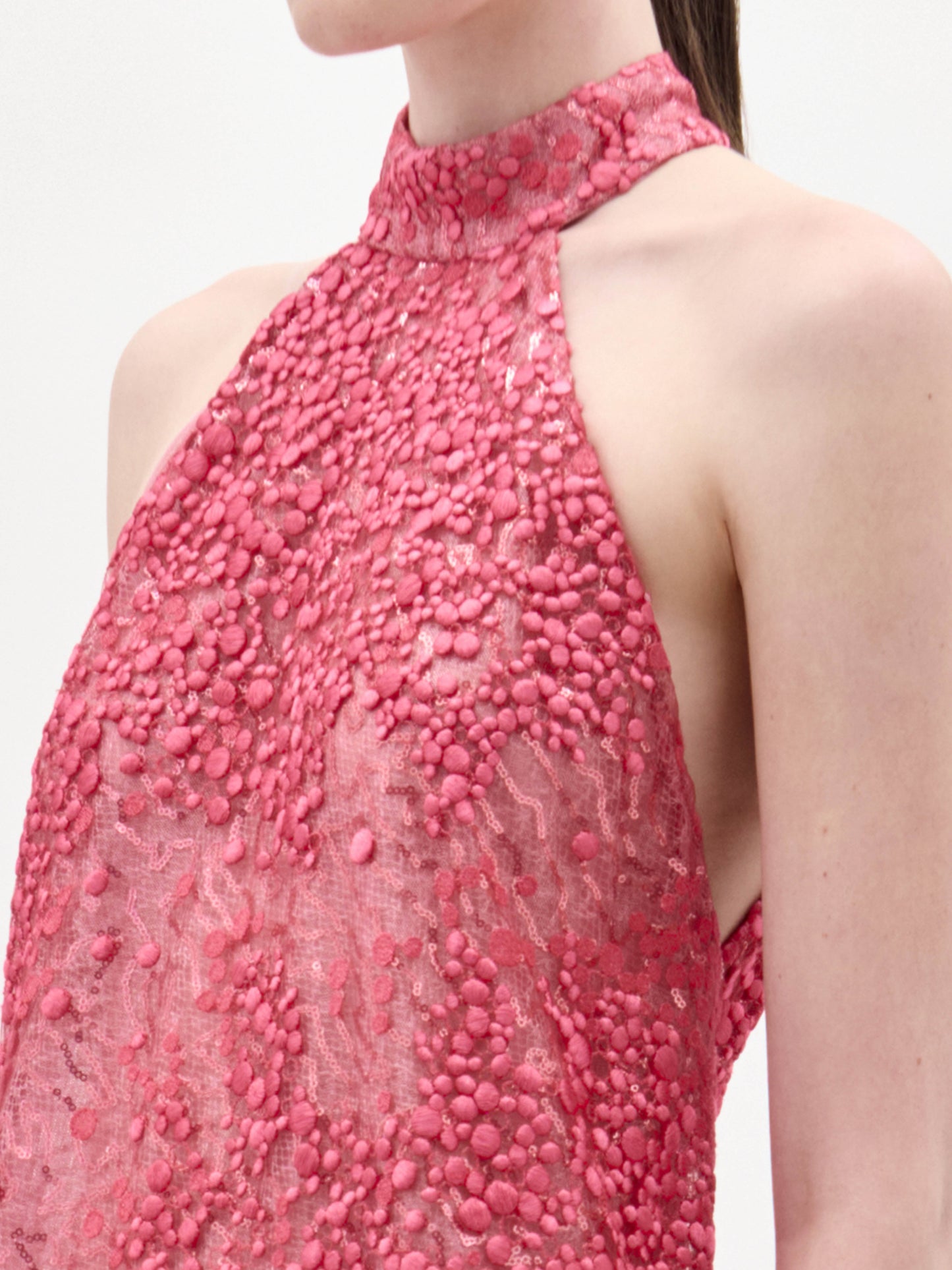 Una persona luce el vestido Tatiana, una prenda rosa sin mangas y de cuello alto con estampado de puntos en relieve. La foto está recortada para mostrar la parte superior del pecho, el hombro y parte de la cara sobre un fondo liso.