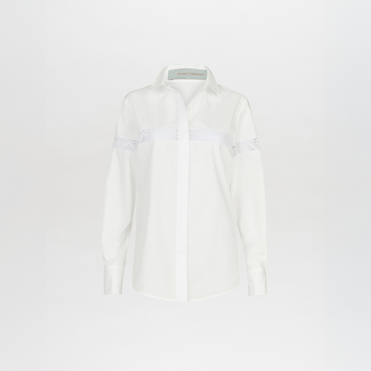 La blusa Andrea White es una blusa blanca de manga larga que presenta detalles bordados en el pecho y la parte superior de los brazos, sobre un fondo blanco liso.