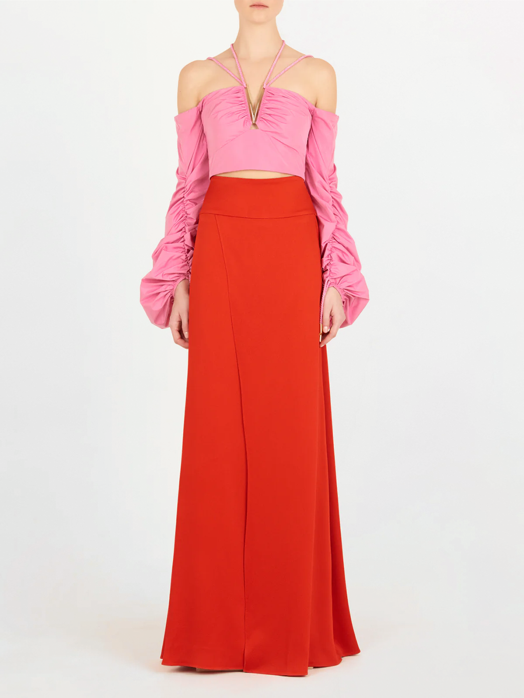 Una persona lleva un crop top rosa sin hombros con mangas fruncidas y escote de tirantes, combinado con la falda de talle alto Pinar Rouge, sobre un fondo blanco liso.