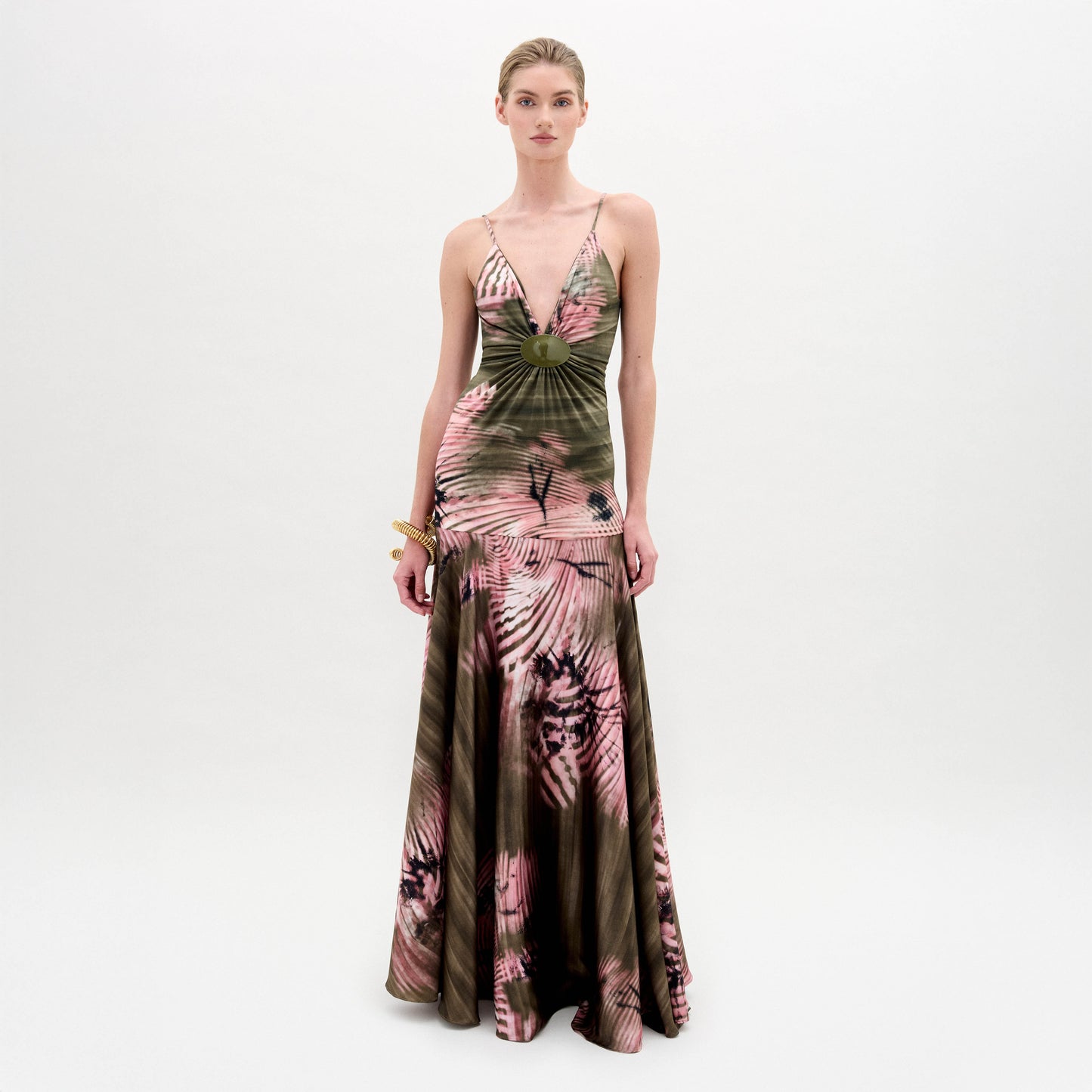 Sobre un fondo blanco liso, una mujer luce el vestido Carmin, un maxi vestido con escote en V y un vibrante estampado rosa y verde. Lleva el pelo recogido y una sencilla pulsera dorada como accesorio.