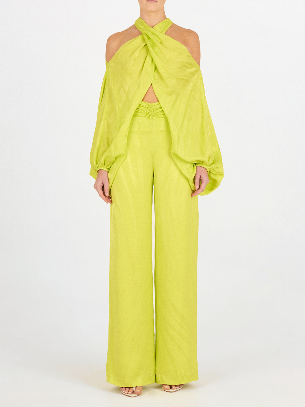 Una persona, de pie y de frente sobre un fondo blanco, lleva el Pantalón Casey Verde Lime, un pantalón de talle alto y pernera ancha en verde lima, combinado con un top sin hombros y zapatos abiertos.