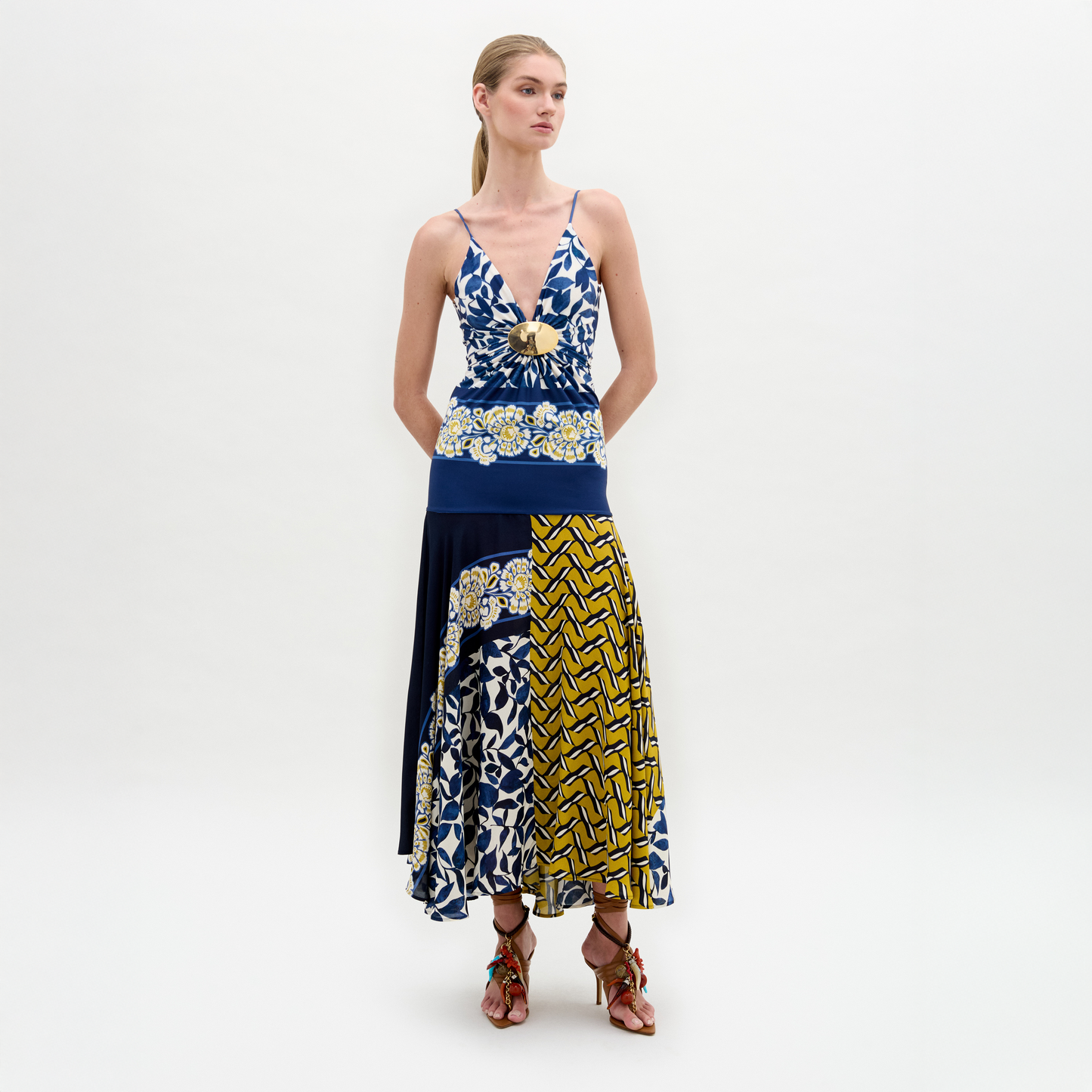 Sobre un fondo blanco, una mujer con el pelo hacia atrás luce el vestido Casiana, un modelo midi de corte ajustado y estampado mixto en azul, amarillo y blanco con escote en pico y falda acampanada, combinado con sandalias de tacón de tiras.