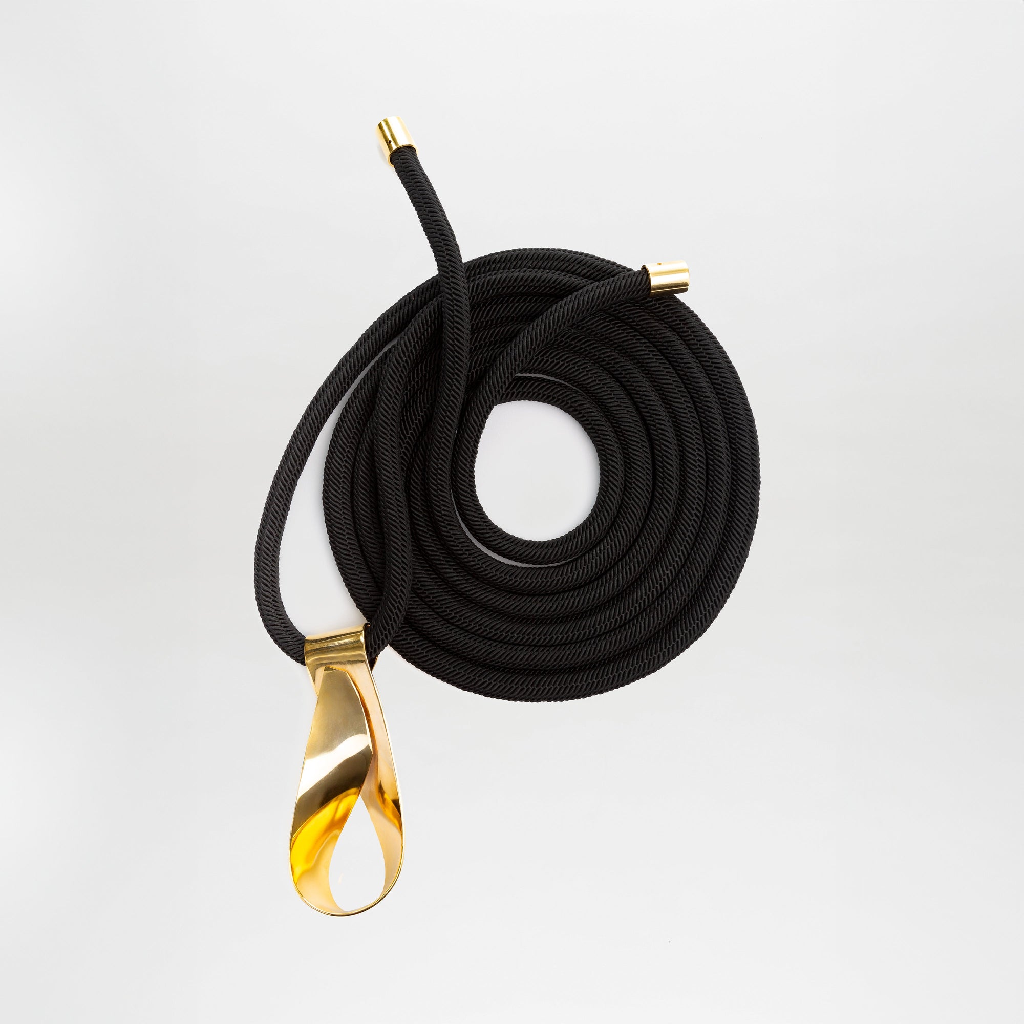 El Cinturón Daiana es un cinturón de cordón negro enrollado con tapones de metal dorado en cada extremo y una hebilla dorada pulida, sobre un fondo blanco liso.