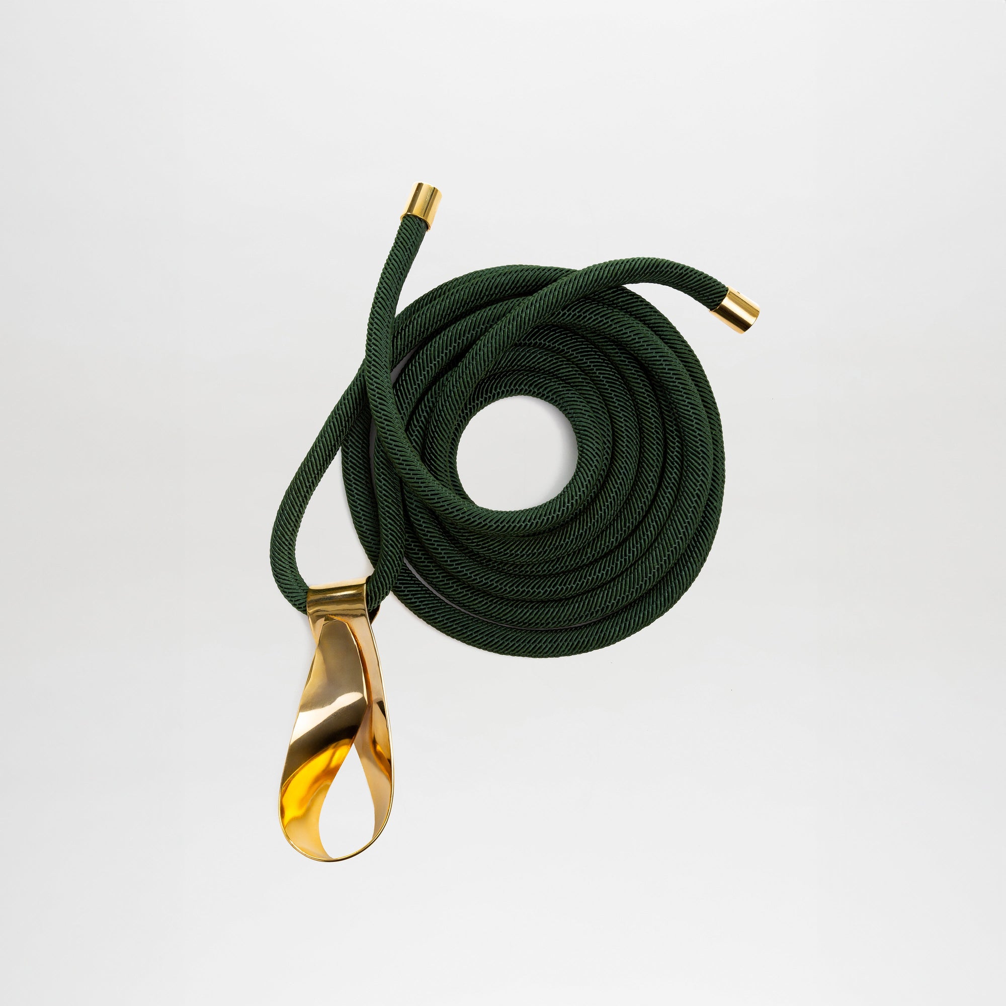 El cinturón Daiana es un cinturón de cordón enrollado de color verde oscuro con tapones metálicos dorados en ambos extremos y una gran hebilla dorada brillante en un extremo, que se muestra sobre un fondo blanco liso.