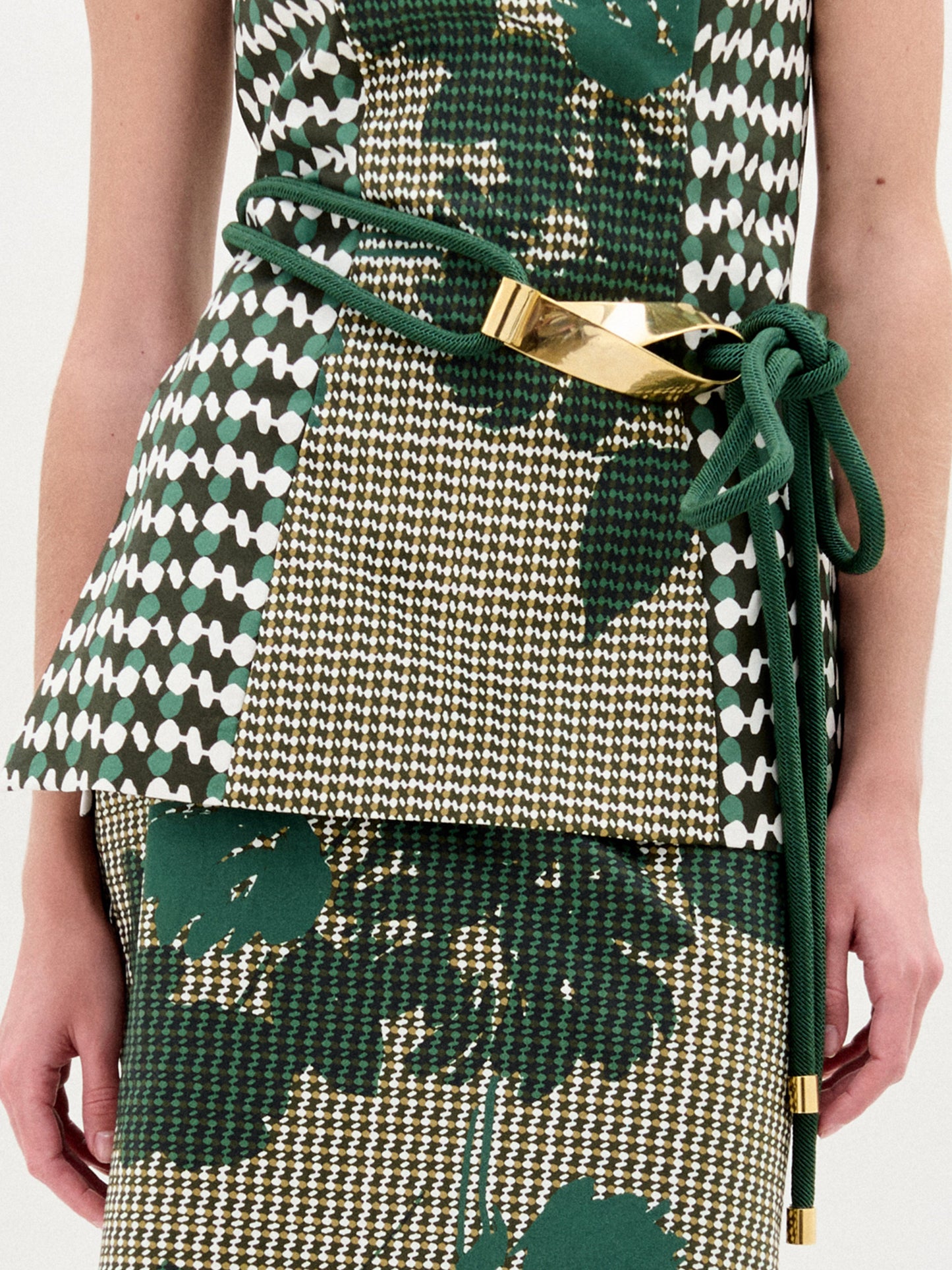 Persona vestida con un traje estampado en verde y blanco, con el cinturón Daiana -con detalles dorados metálicos- atado a la cintura. Sólo se ve el torso y parte del brazo. Este llamativo look está hecho en Colombia.