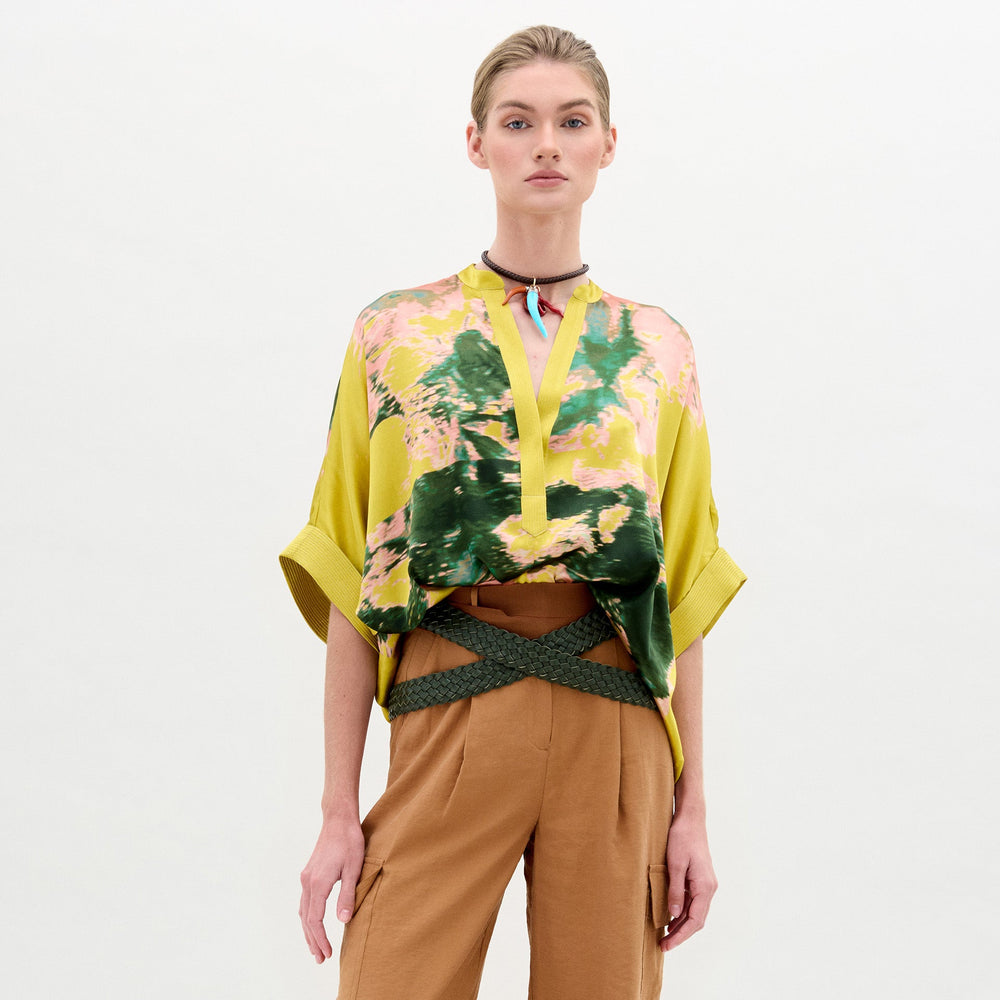 Una persona con la blusa Daia suelta en amarillo-verde de tela italiana, mangas anchas, pantalón beige de tiro alto, cinturón trenzado y gargantilla posa ante fondo blanco. Hecho en Colombia.