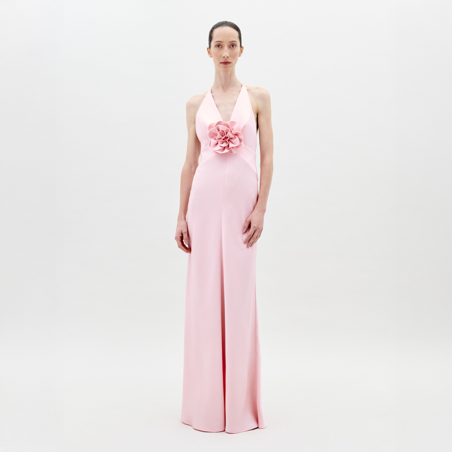 Una persona posa sobre fondo blanco luciendo el Vestido Daniela, un maxi vestido de textil italiano rosa pálido con escote halter y gran motivo floral en la cintura.
