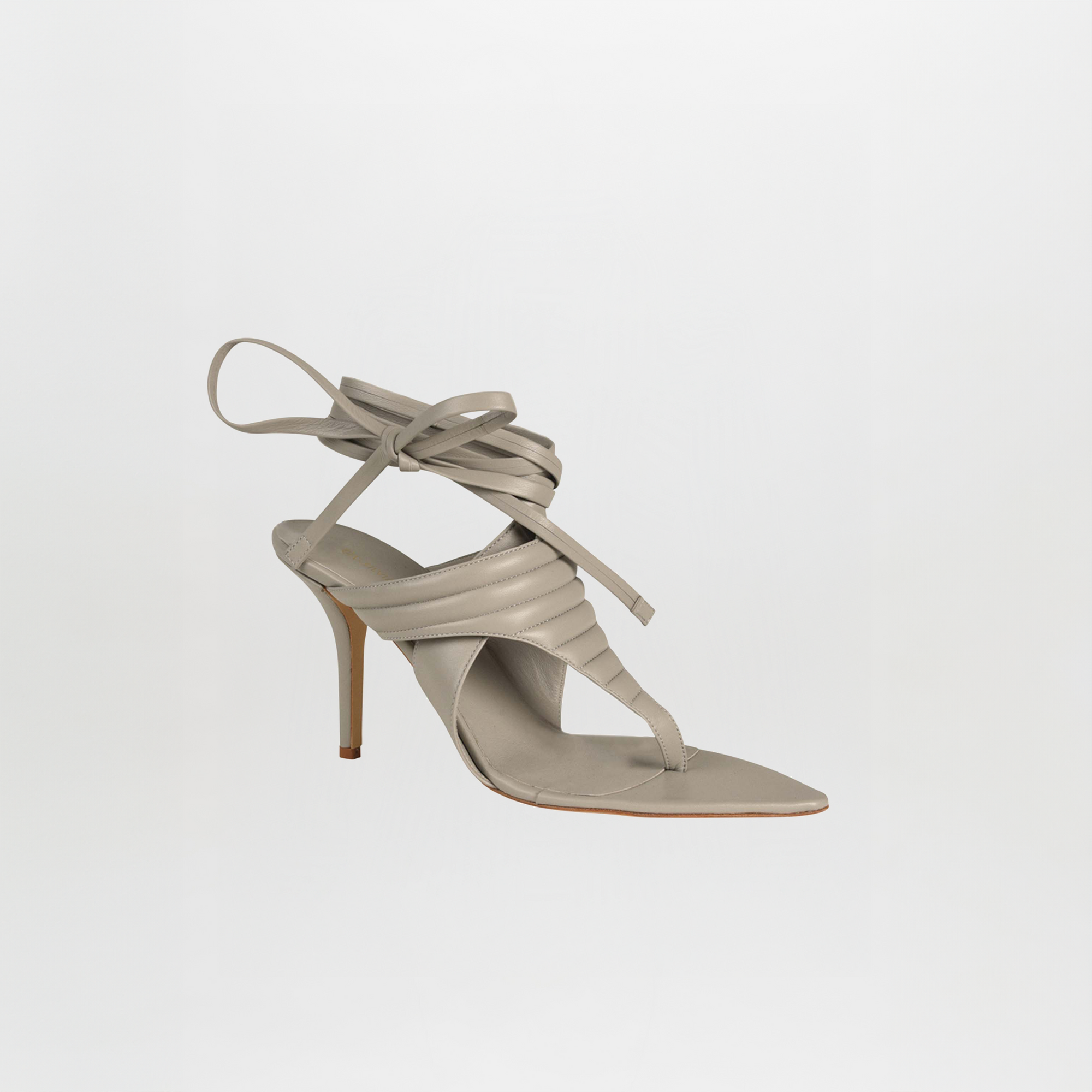 Tacones Dalila Gris es una sandalia de tacón alto de un solo color topo con un fino tacón de aguja, punta cuadrada, tiras acolchadas y cordones que rodean el tobillo, que se muestra sobre un fondo blanco liso.