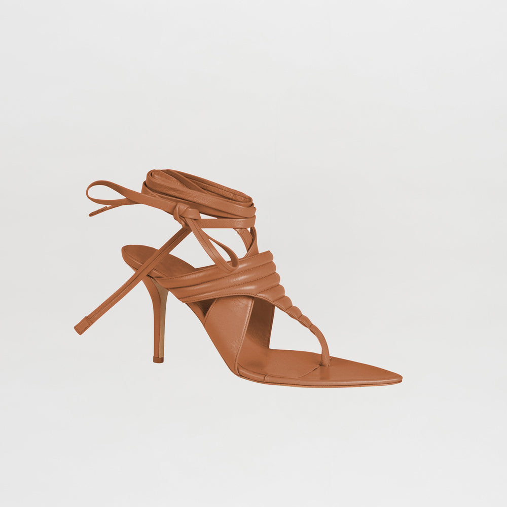 La Tacones Dalila Camel es una sandalia de tacón alto color tostado con punta cuadrada, suela fina, múltiples tiras de cuero, cordones que rodean el tobillo y una tira en la punta, que se muestra sobre un fondo blanco liso.